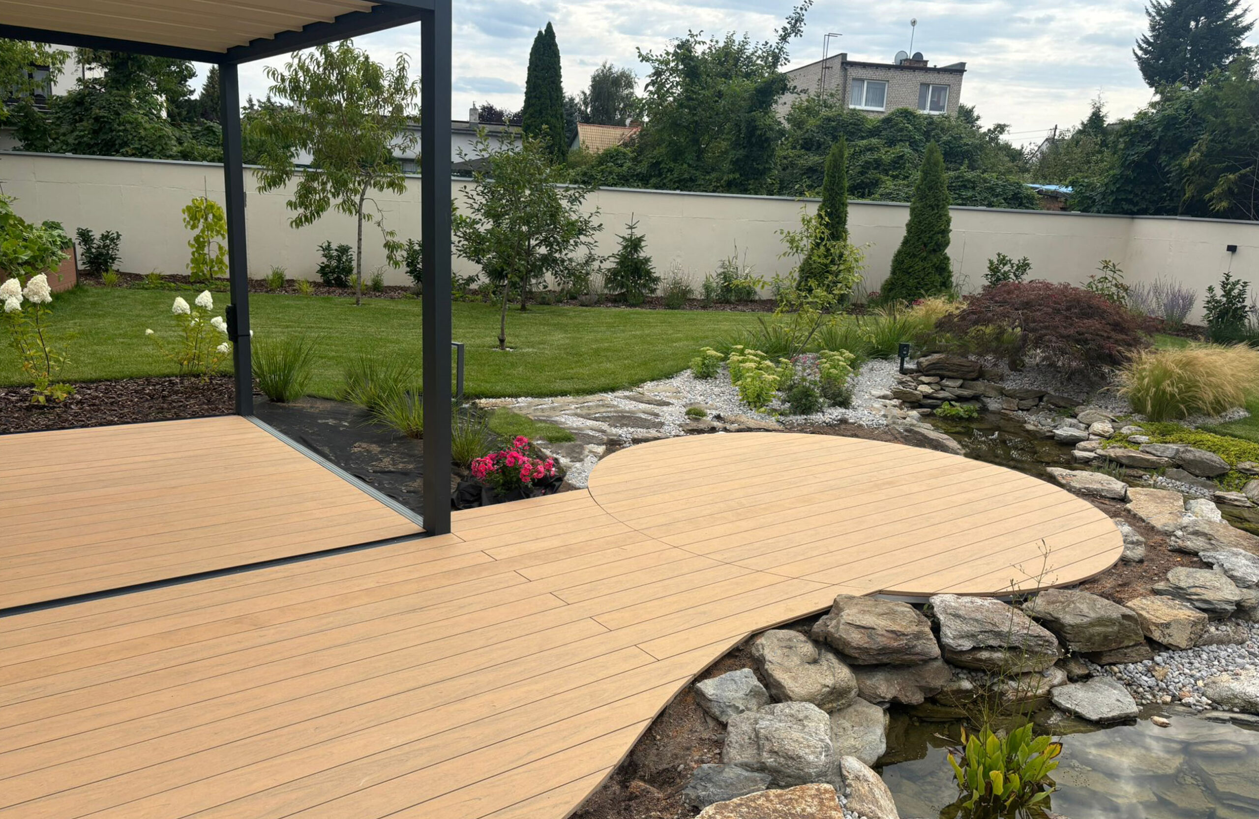 BRUGGAN Multicolor sand decking with a custom curved design beside a landscaped garden pond