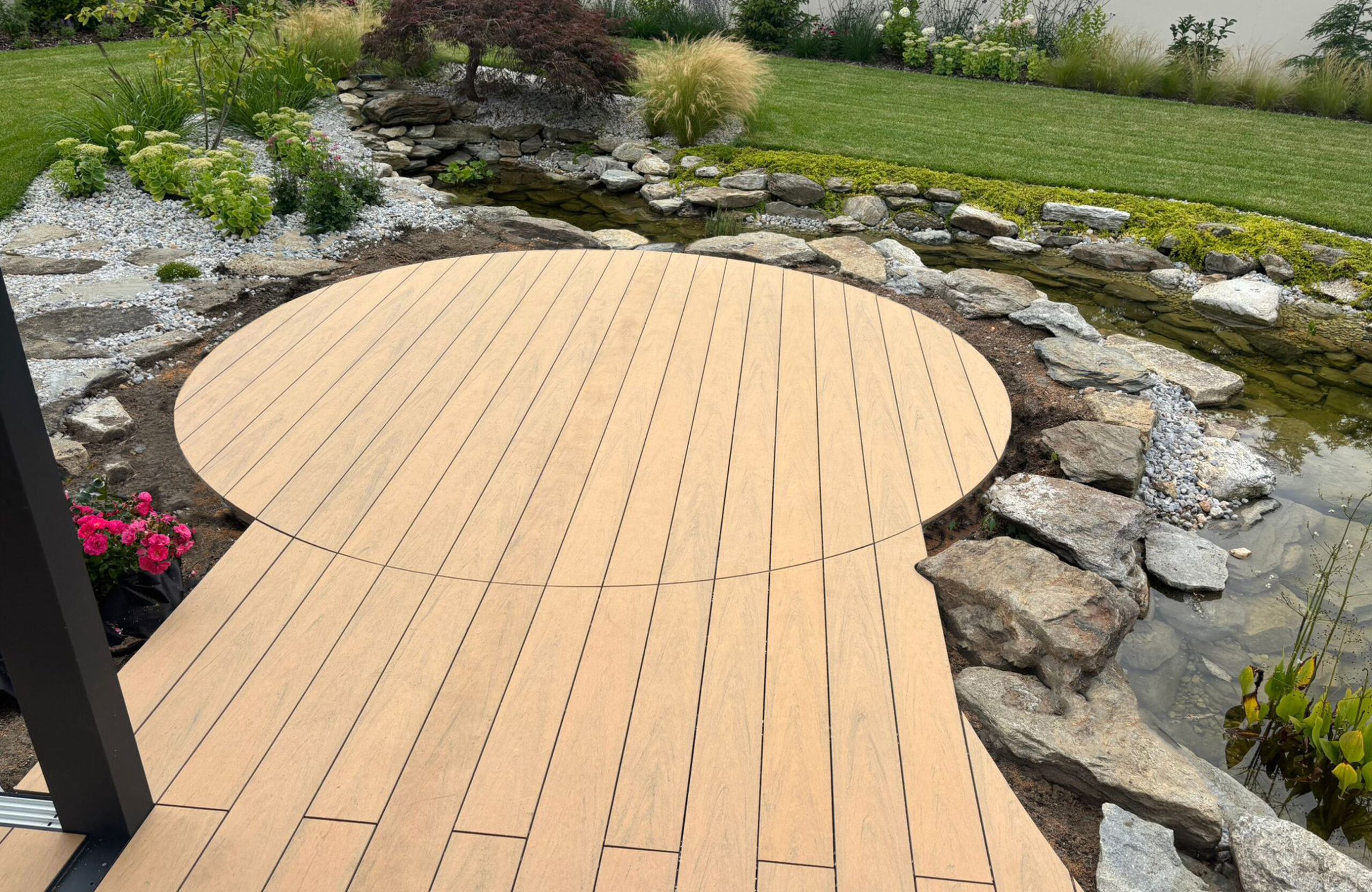 BRUGGAN Multicolor sand decking with a custom curved design beside a landscaped garden pond
