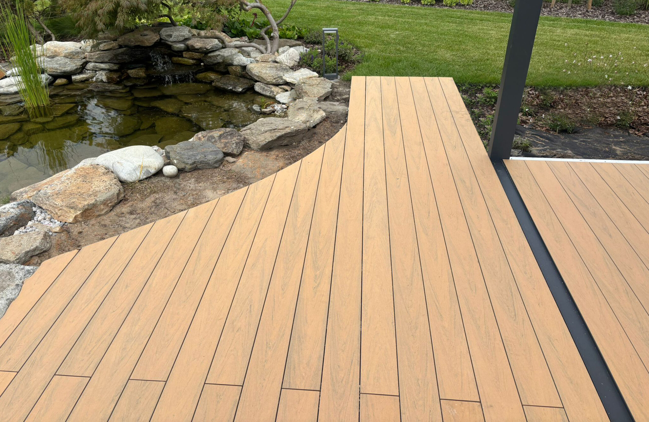 BRUGGAN Multicolor sand decking with a custom curved design beside a landscaped garden pond