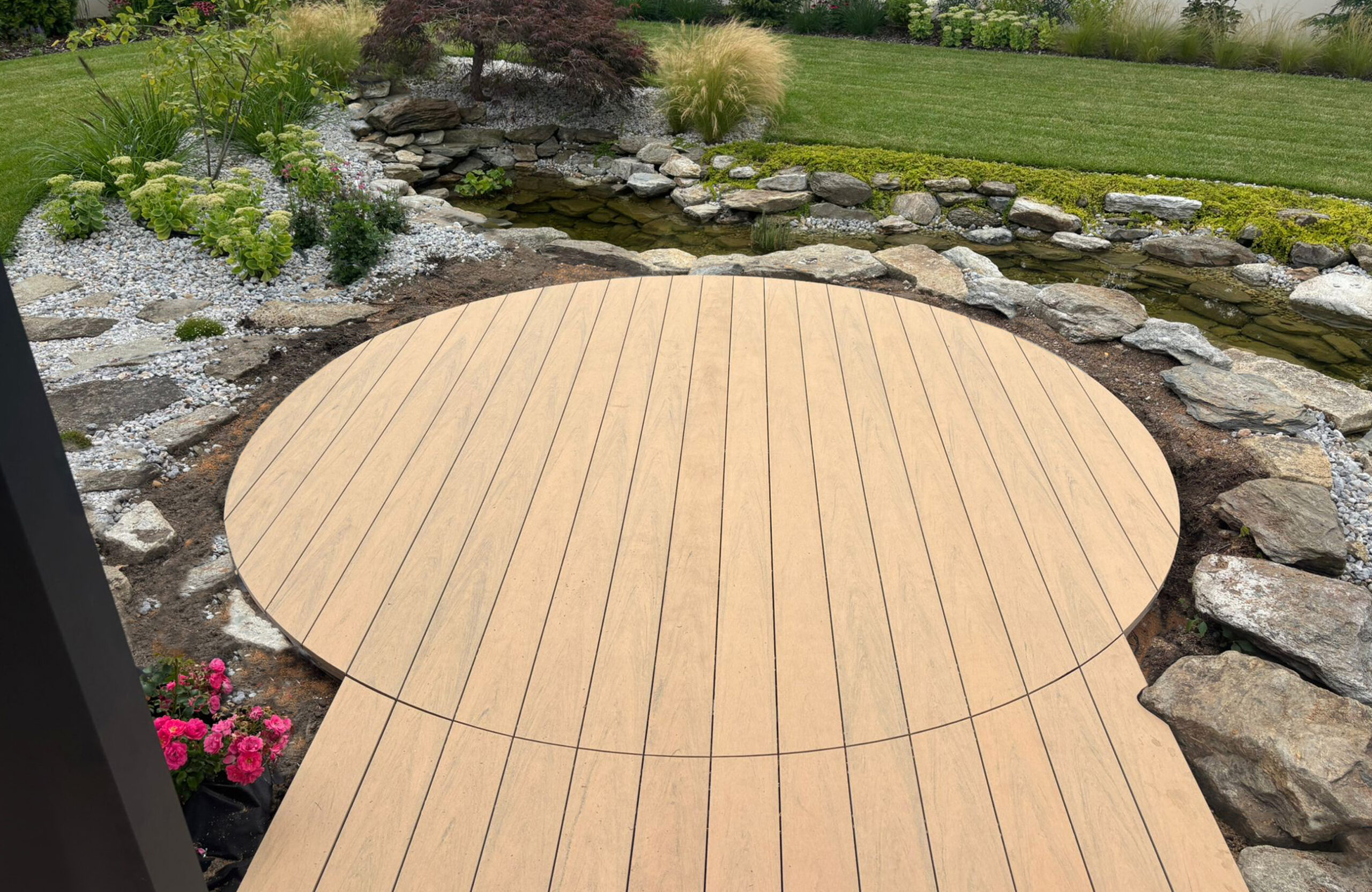 BRUGGAN Multicolor sand decking with a custom curved design beside a landscaped garden pond