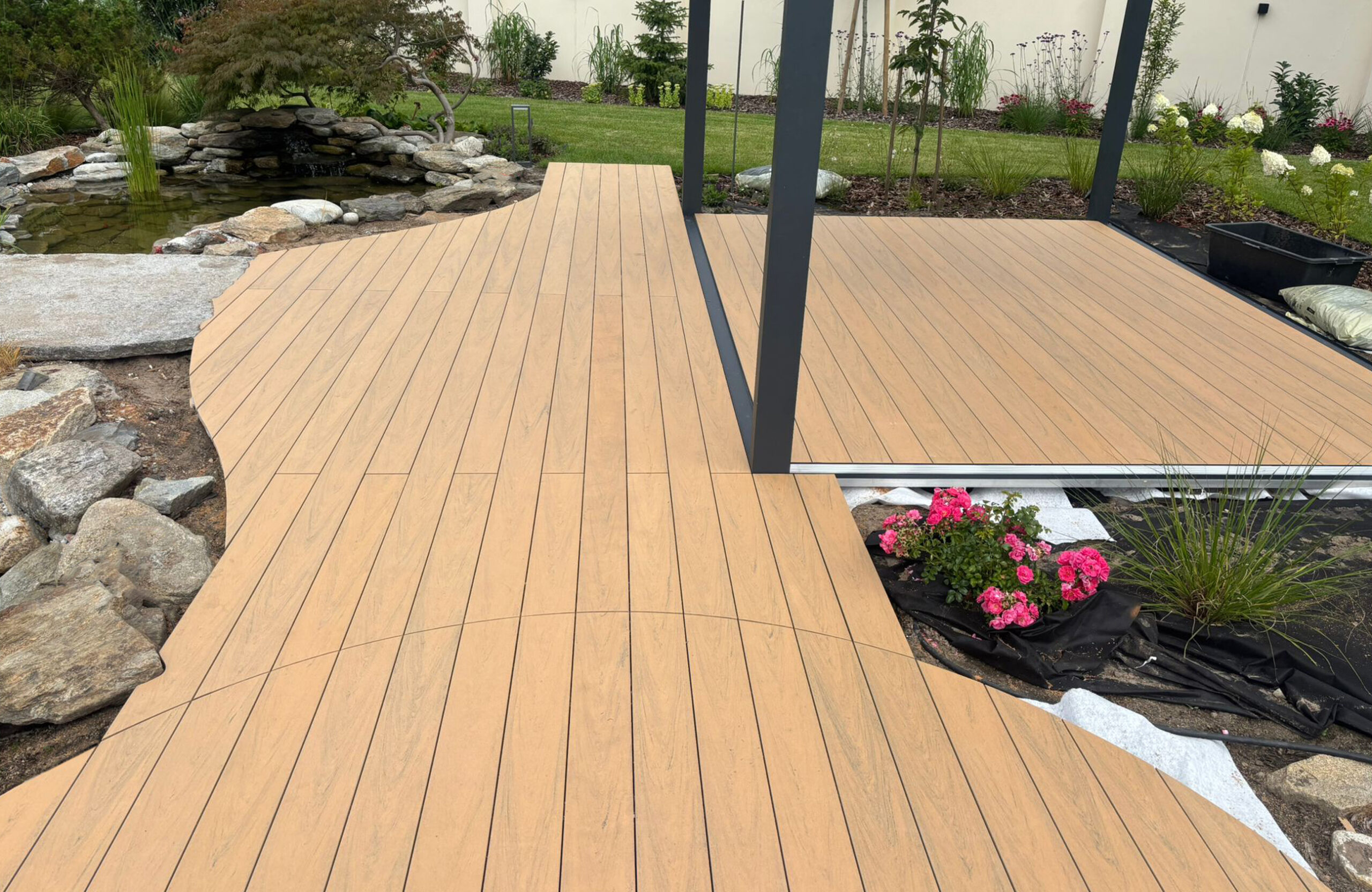 BRUGGAN Multicolor sand decking with a custom curved design beside a landscaped garden pond