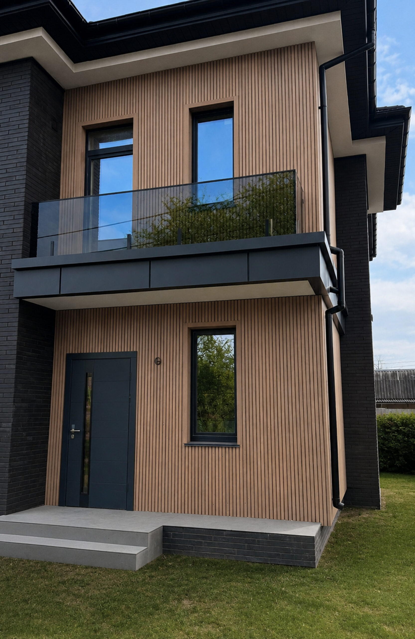Modern two-story house with vertical brown siding, dark brick accents, and a glass-railed balcony.