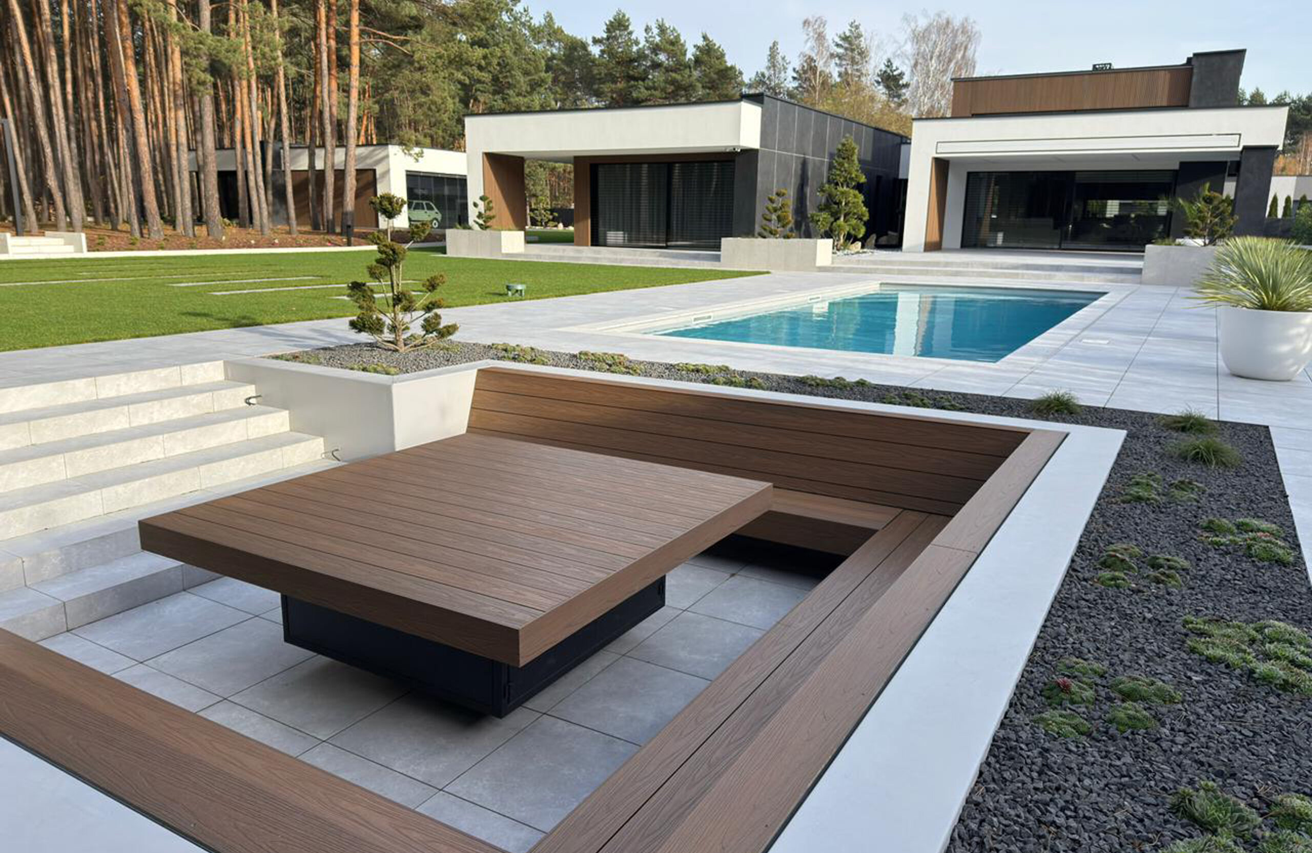 Modern luxury backyard with a rectangular pool, white tile deck, and wooden seating areas in front of a contemporary house.
