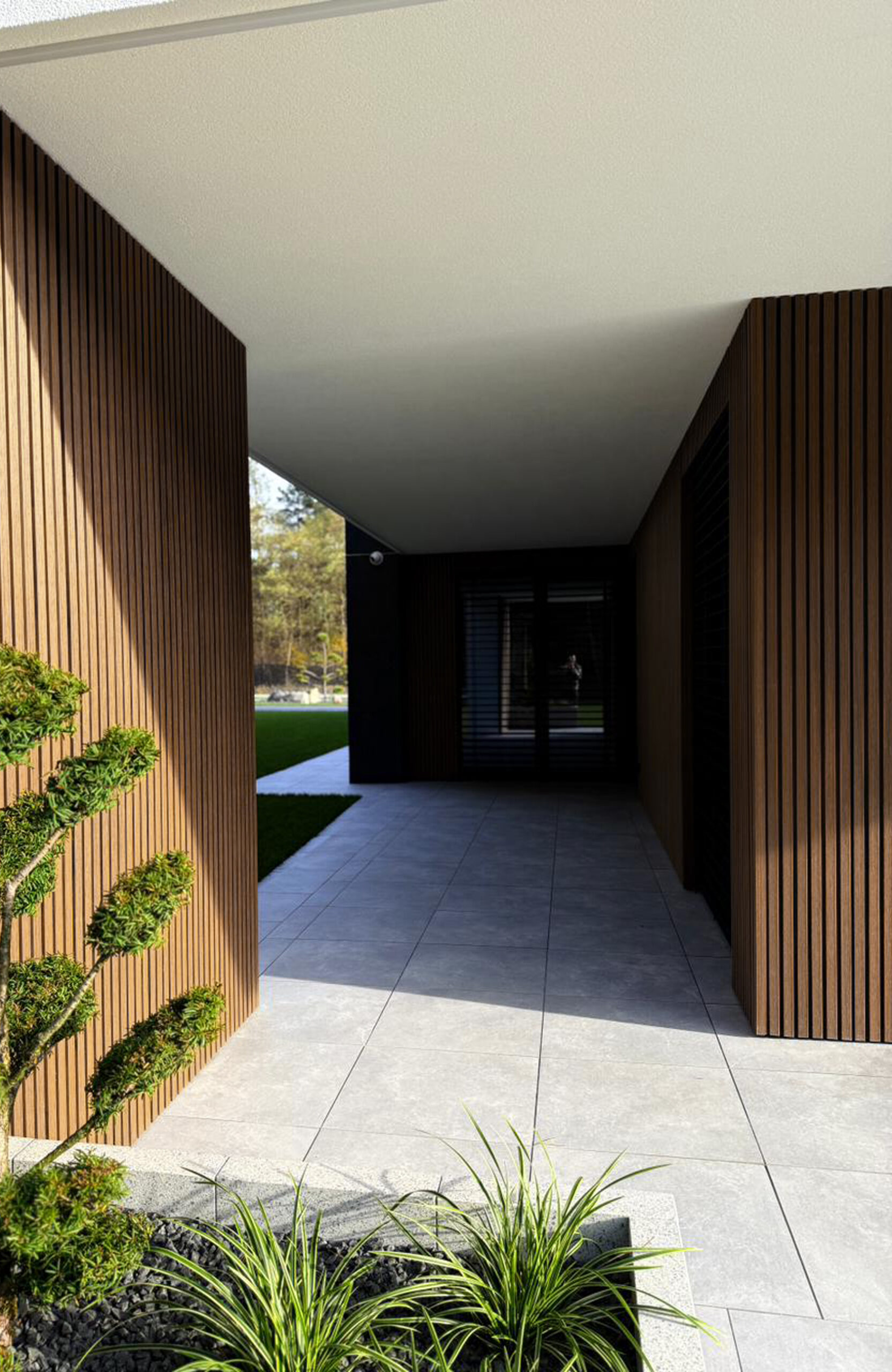 Modern walkway between wooden slat walls with grey tiled floor and landscaping in foreground