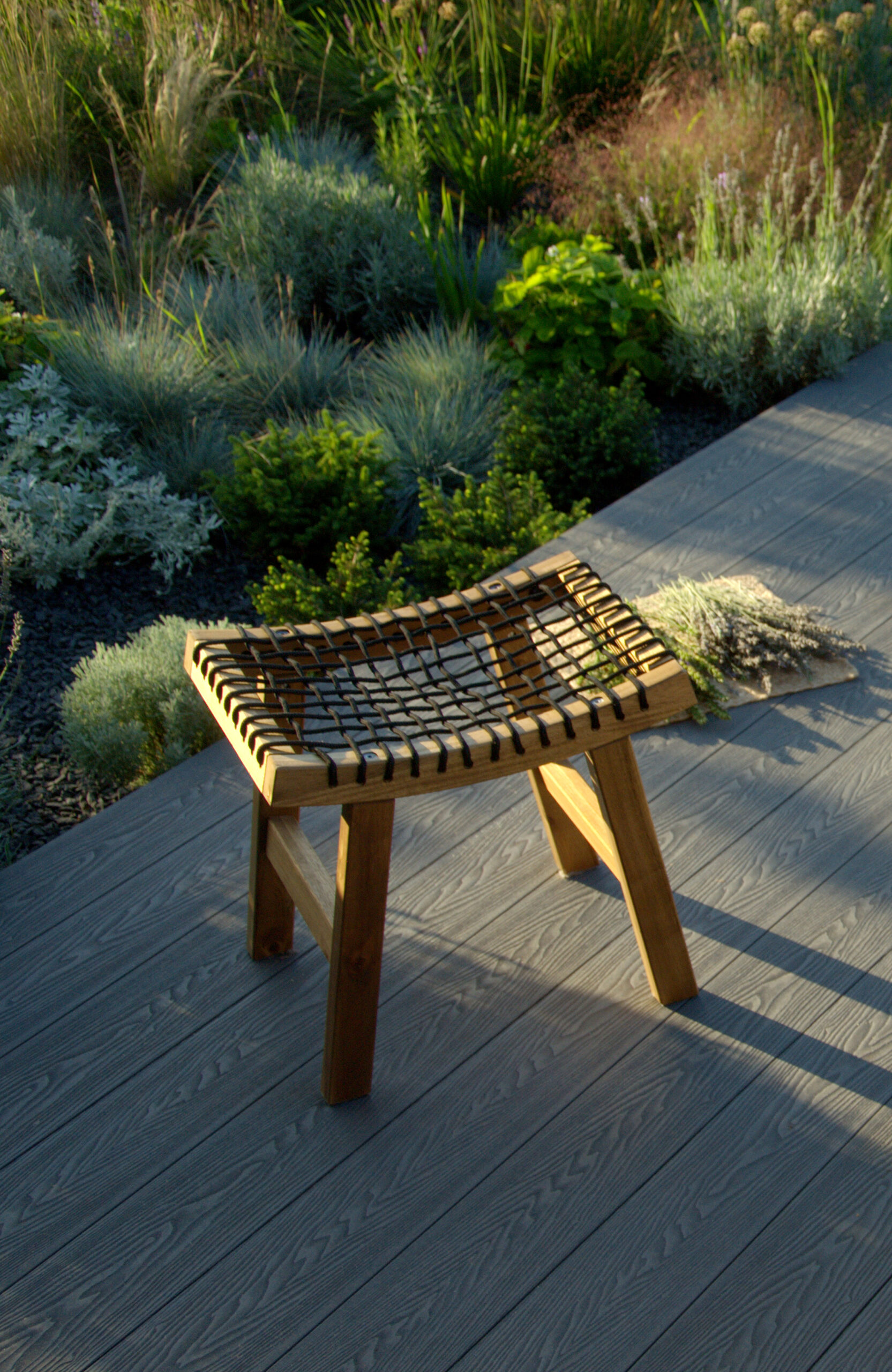 Bruggan Elegant Graphite composite decking terrace with wooden stool surrounded by lush garden plants