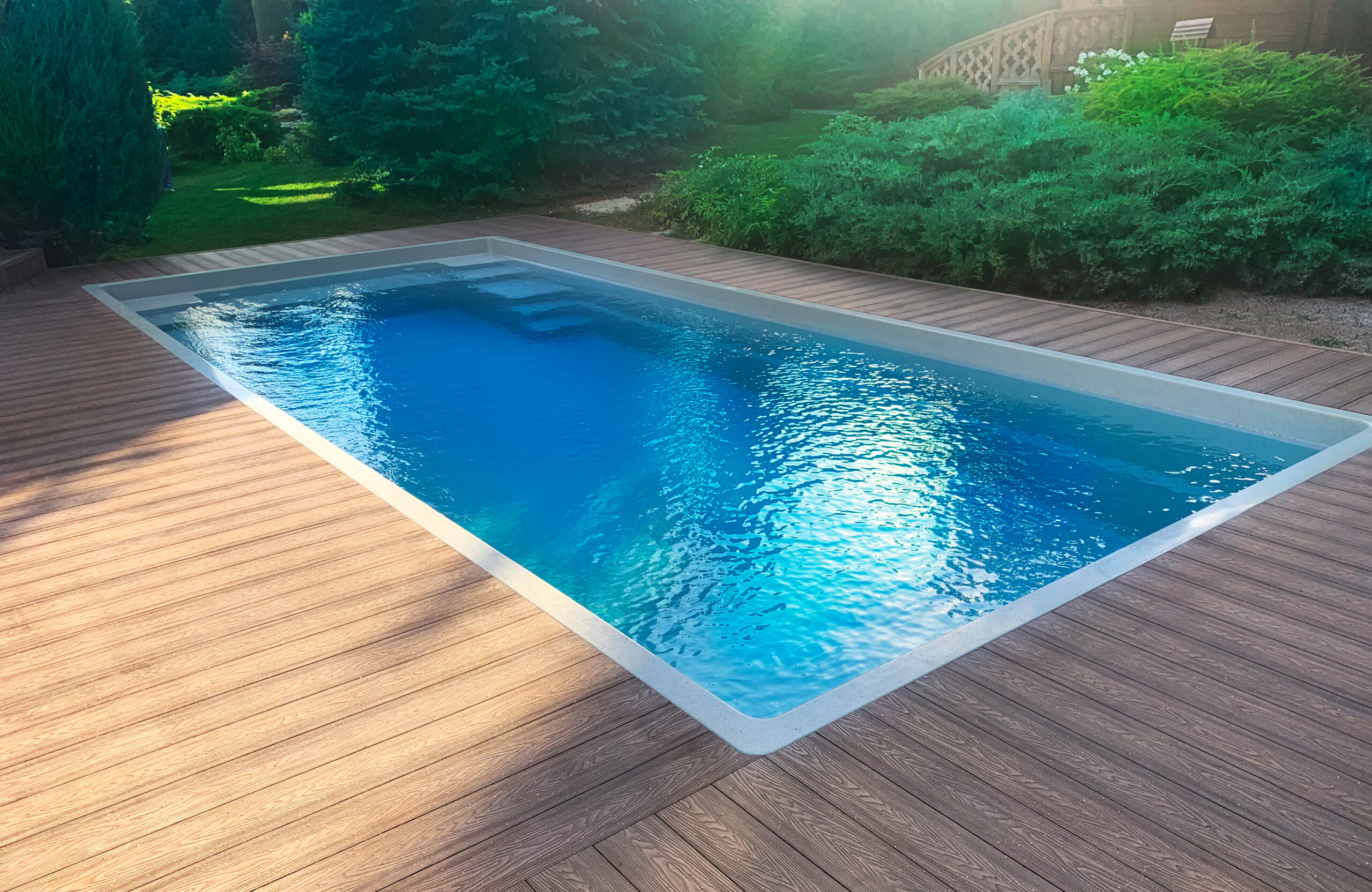 Bruggan Elegant Wine Brown composite decking surrounding a rectangular outdoor swimming pool in a landscaped garden