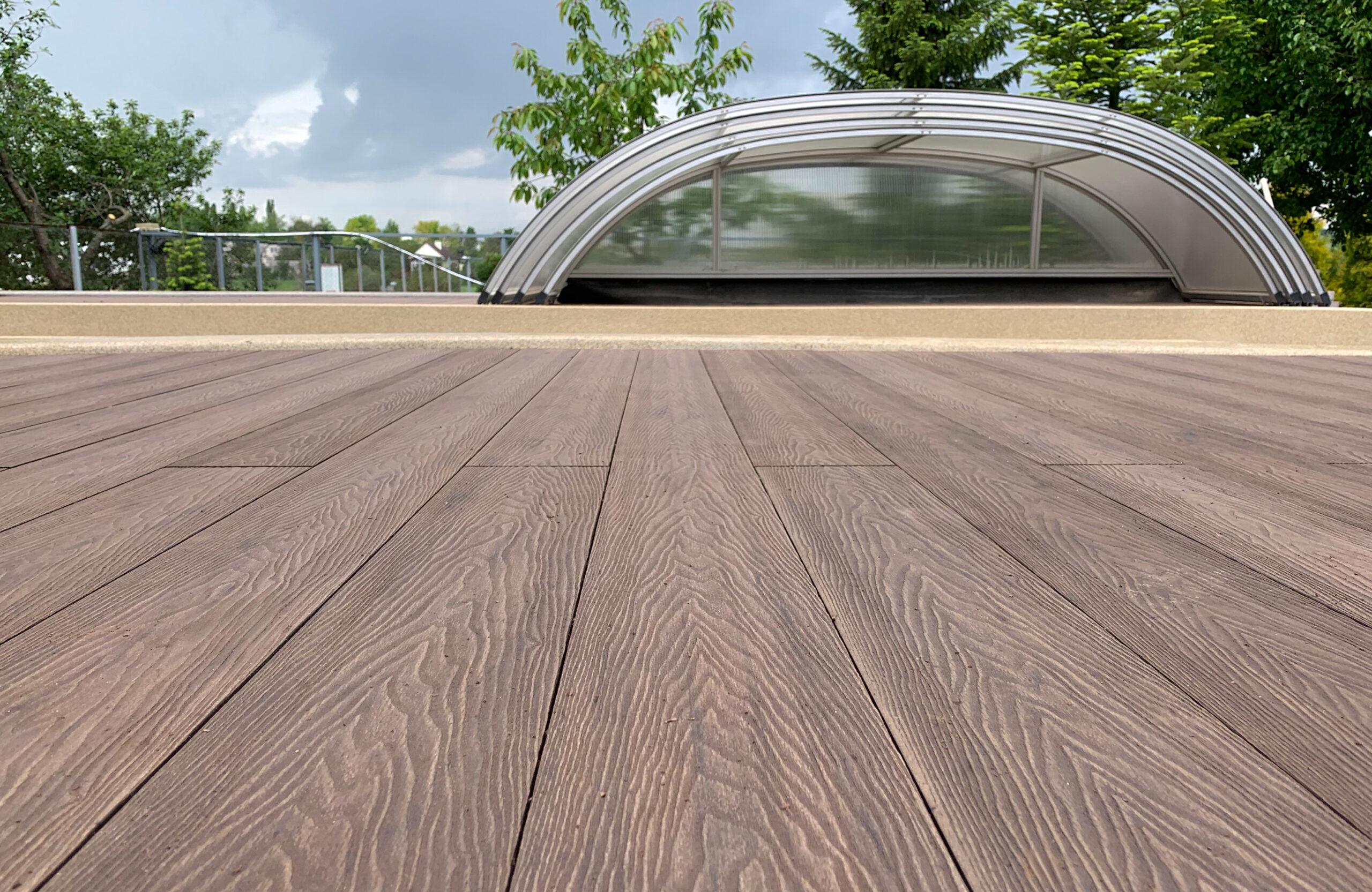 Close-up of Bruggan Elegant Wine Brown composite decking with natural wood grain texture beside a covered swimming pool