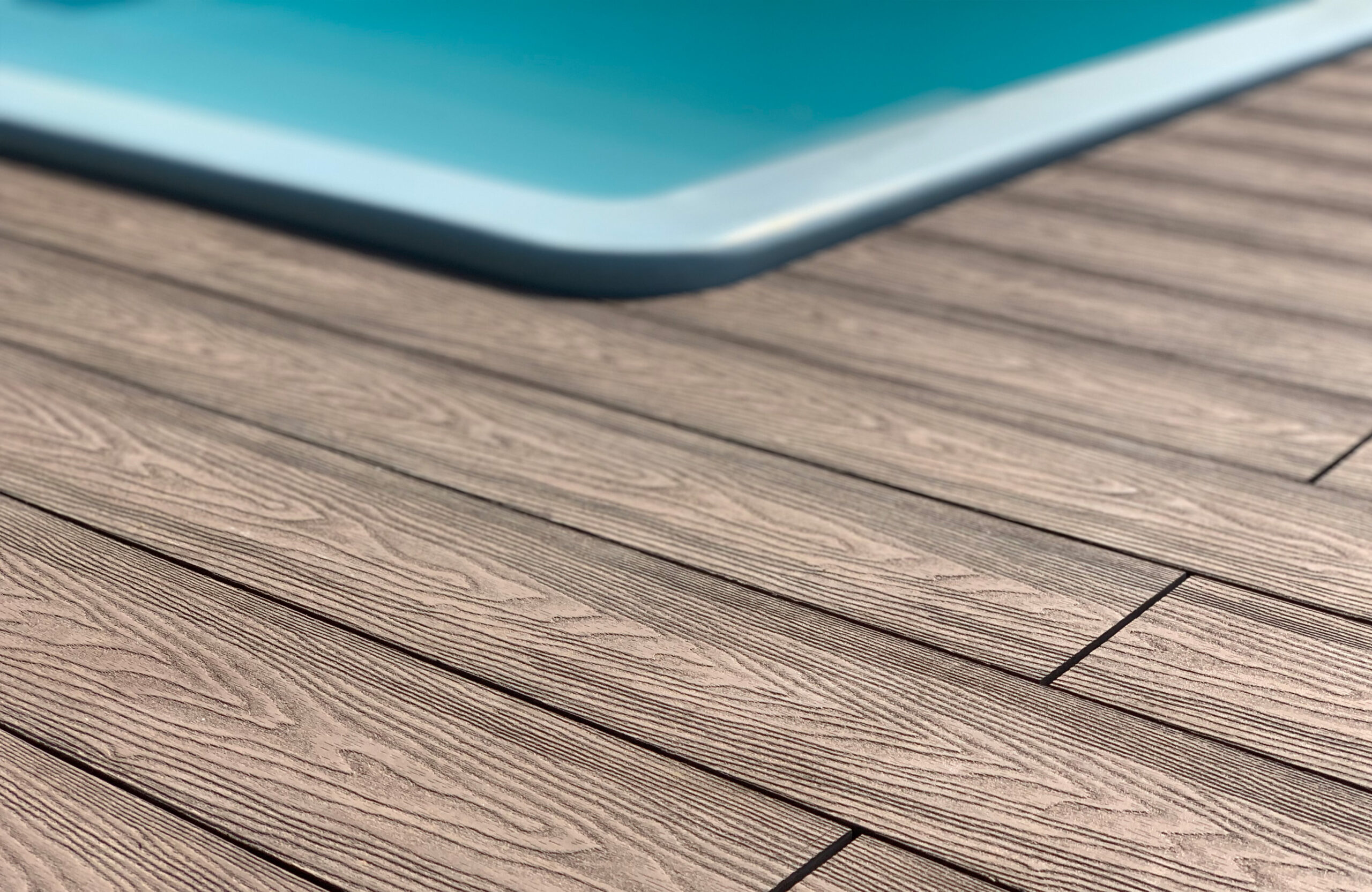 Close-up of Bruggan Elegant Wine Brown composite decking showing detailed wood grain texture beside the pool