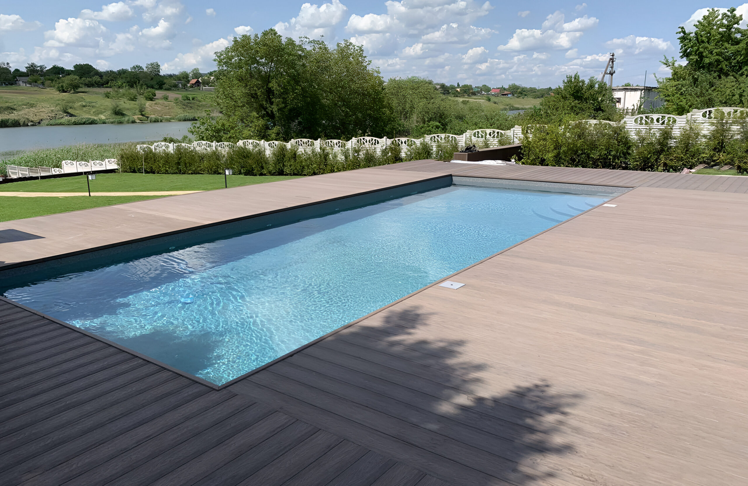Outdoor swimming pool surrounded by Bruggan Elegant Wine Brown composite decking with a scenic lake view