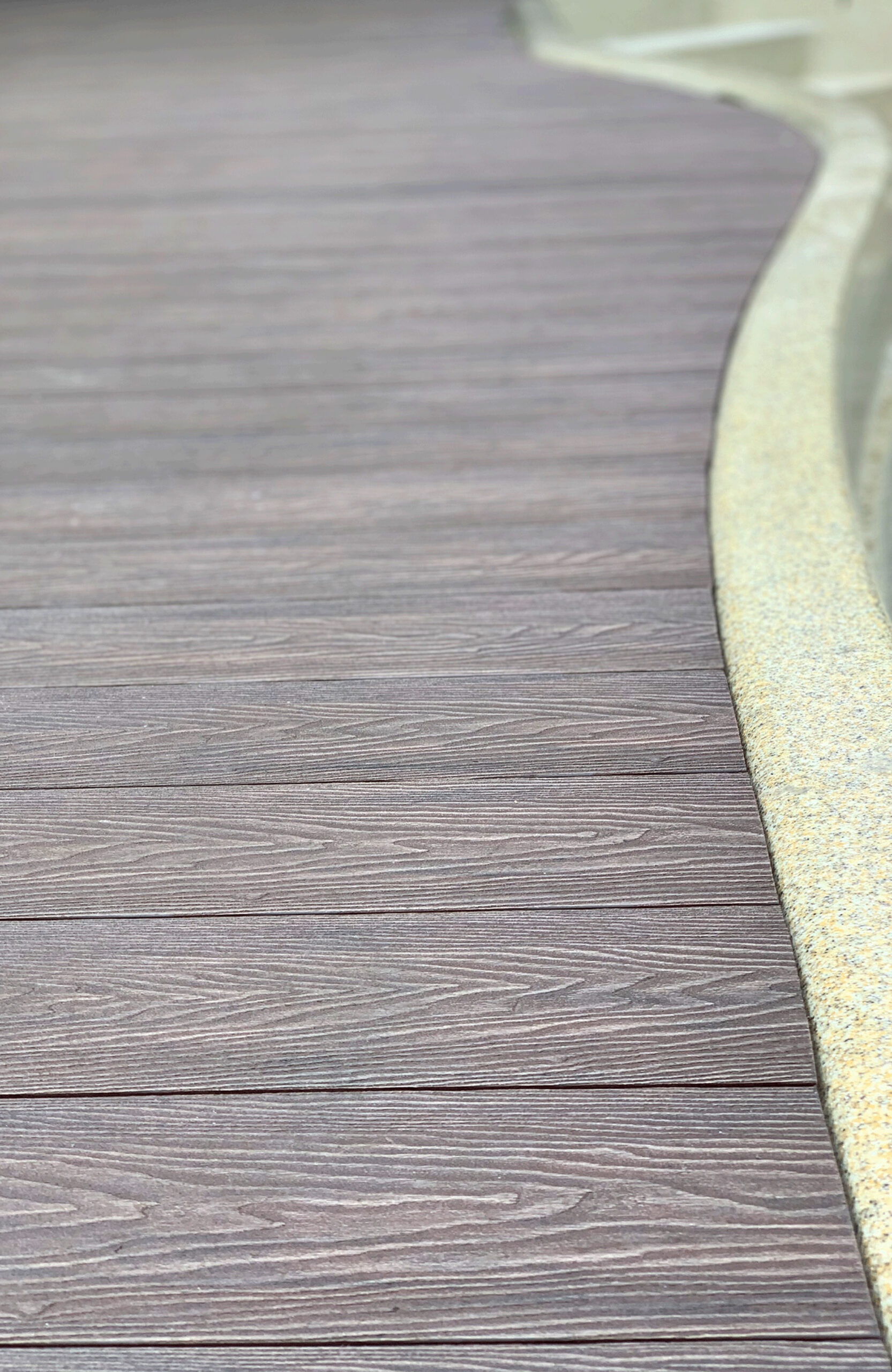 Bruggan Elegant Wine Brown composite decking fitted around the curved edge of a swimming pool