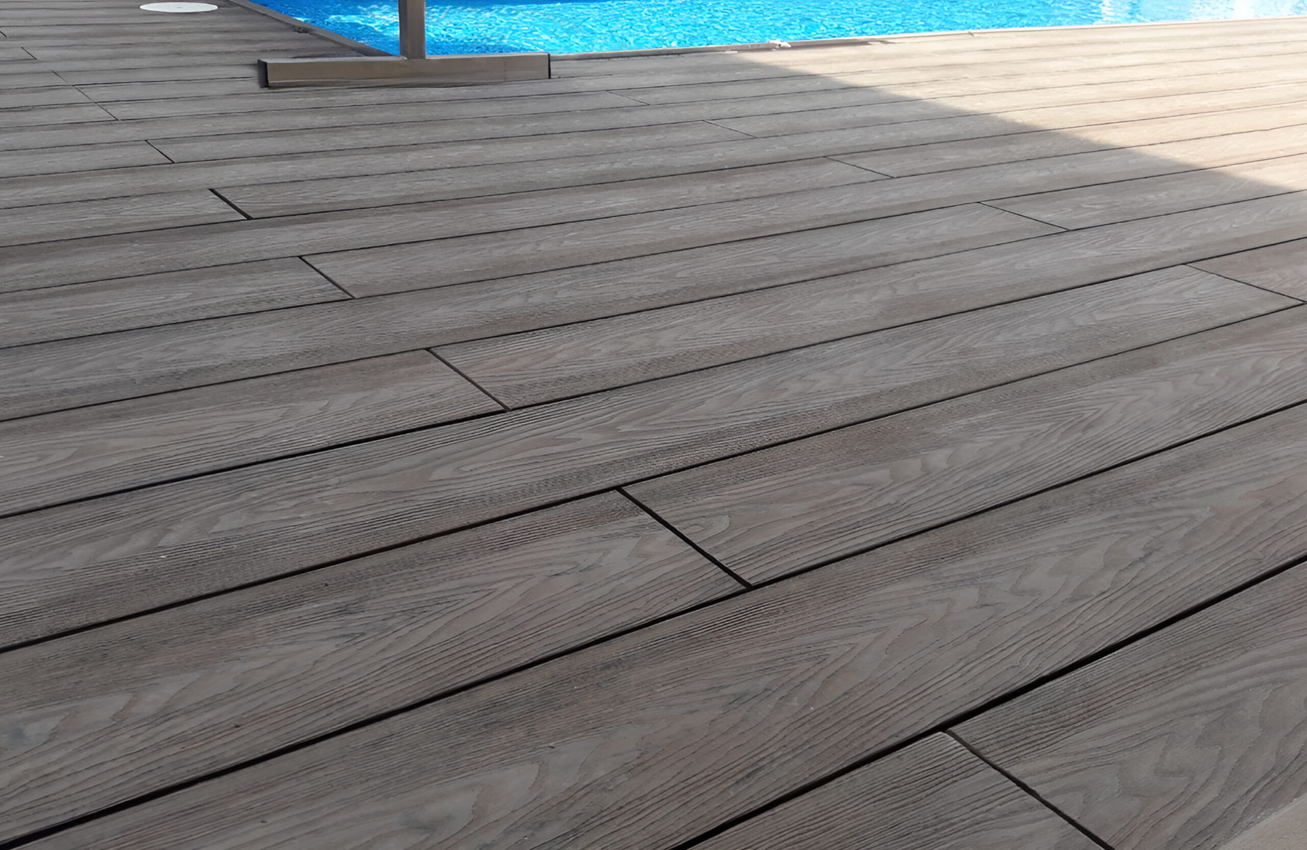 Close-up of Bruggan Elegant Wine Brown composite decking with realistic wood grain texture beside a swimming pool