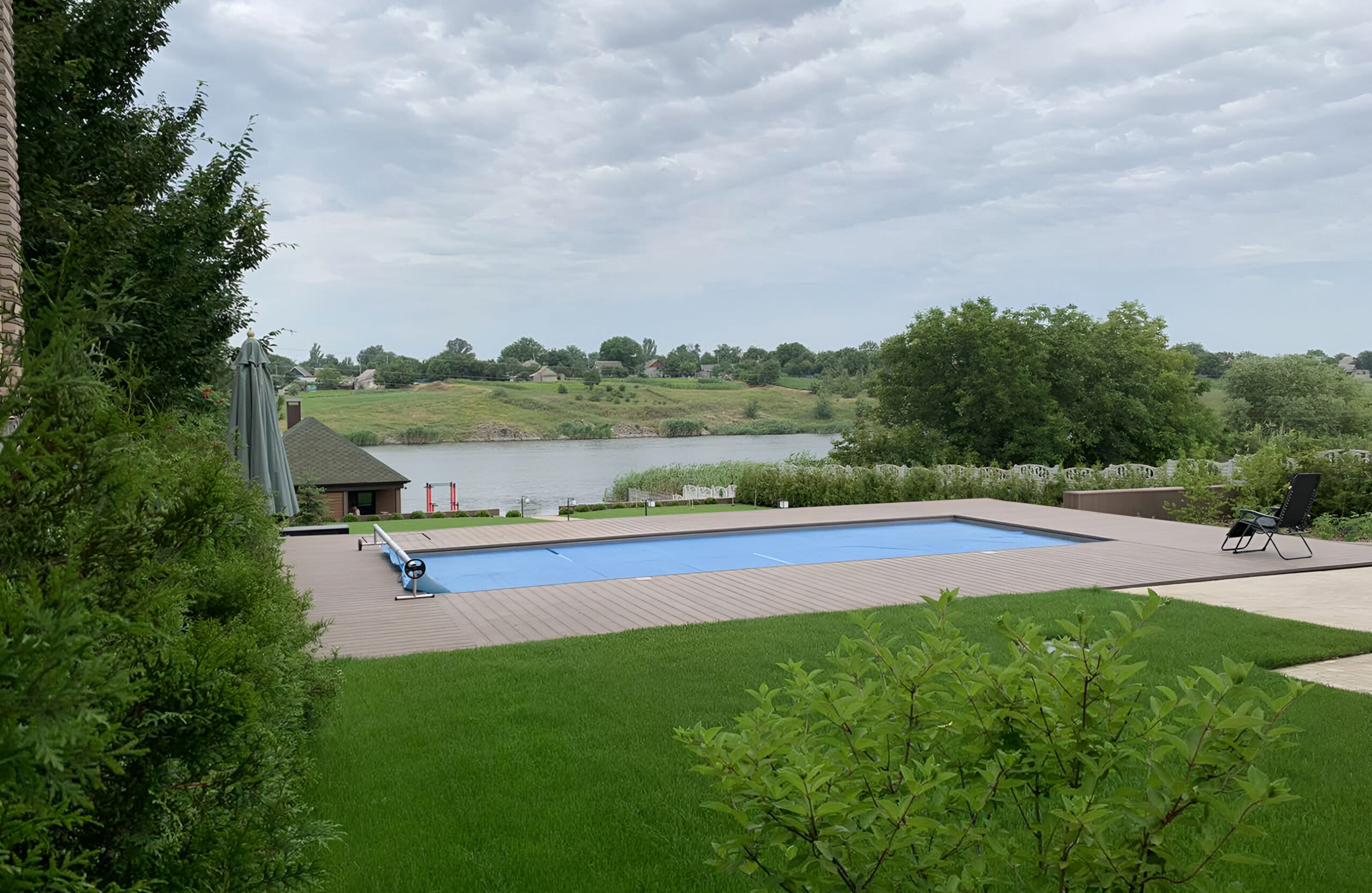 Outdoor swimming pool surrounded by Bruggan Elegant Wine Brown composite decking with a scenic lake view