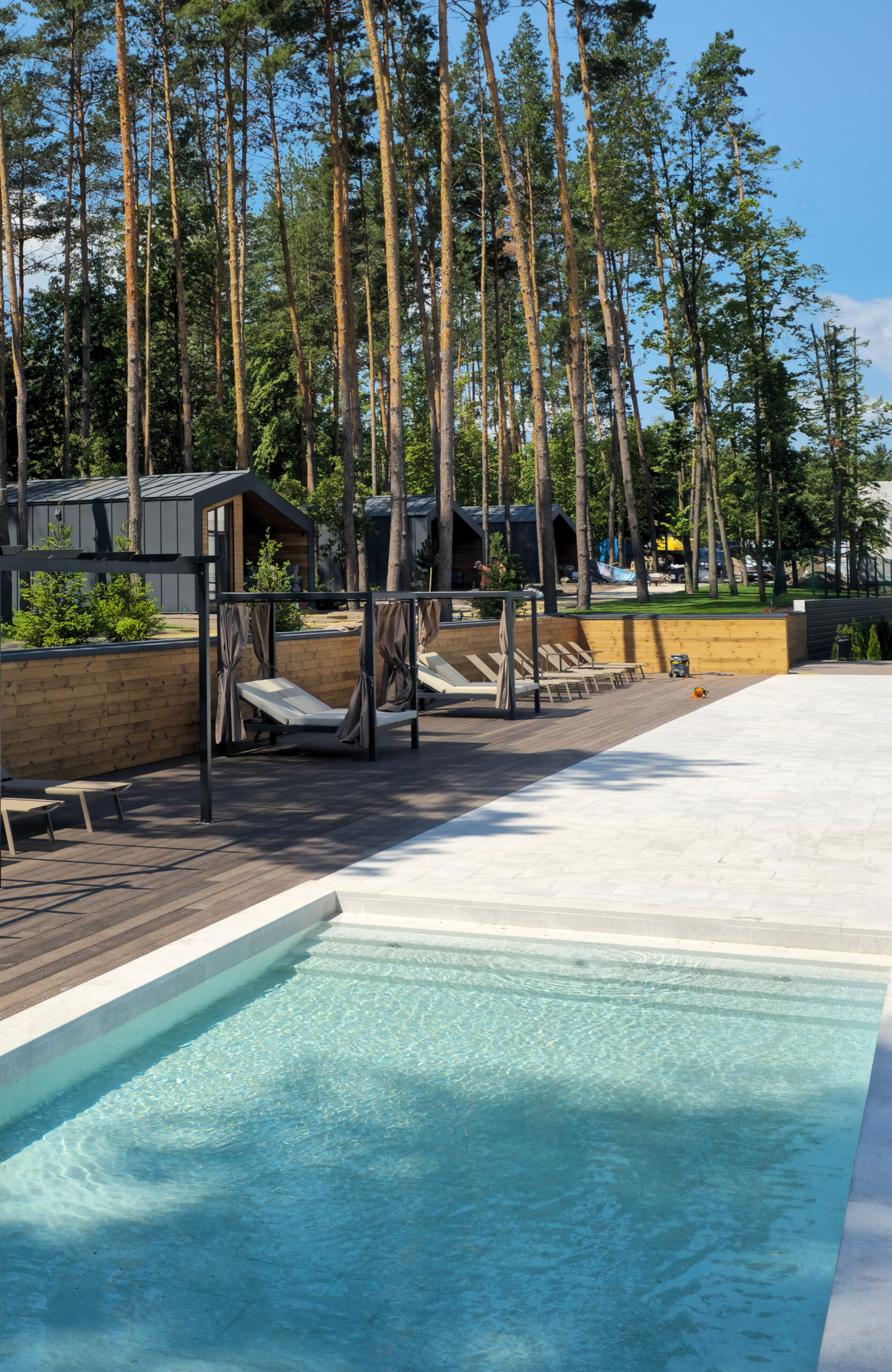 Swimming pool and relaxation area with Bruggan Elegant Wine Brown decking surrounded by pine trees at Riverwood