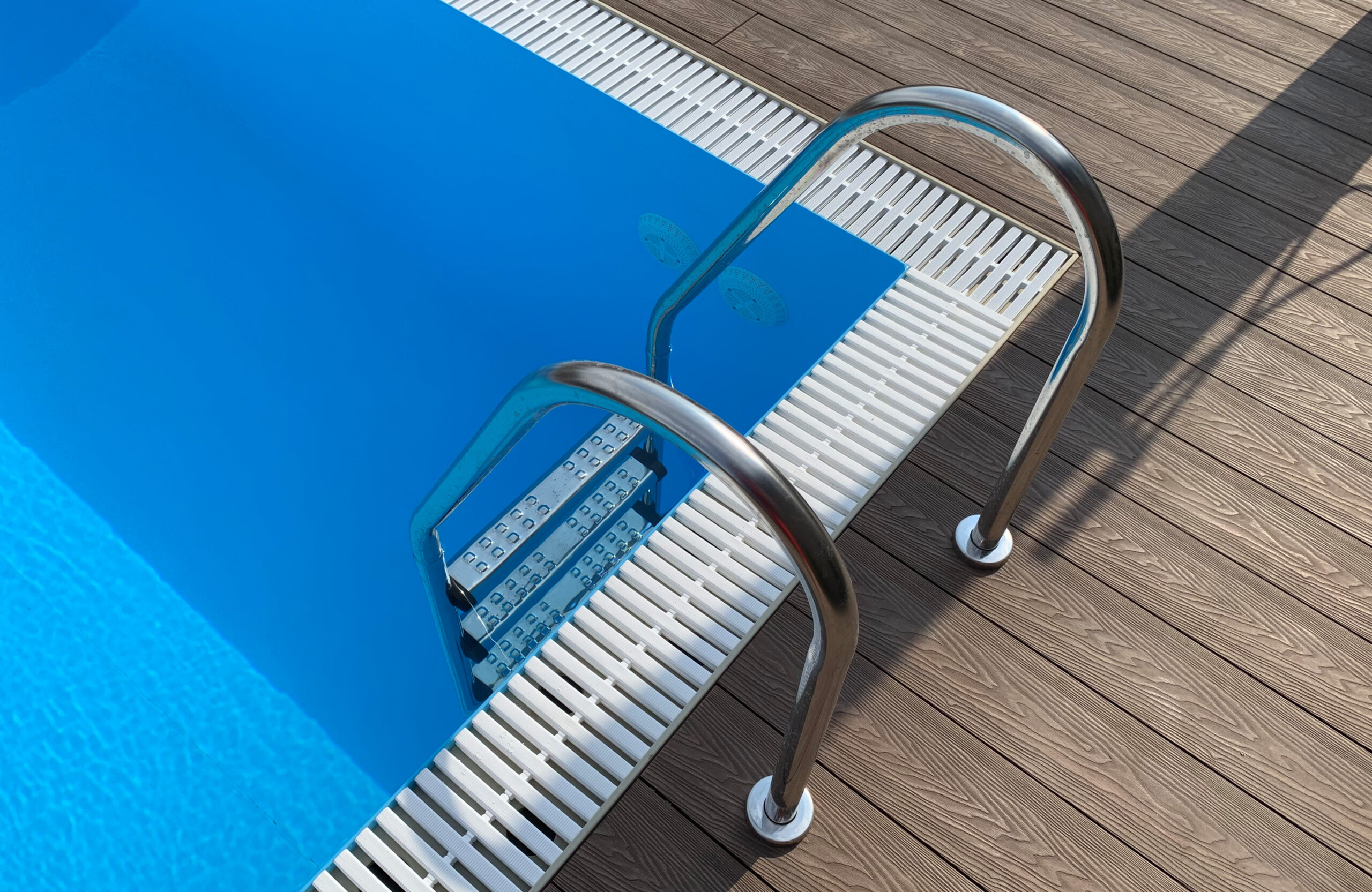 Bruggan Elegant Wine Brown composite decking with stainless steel pool ladder beside an outdoor swimming pool