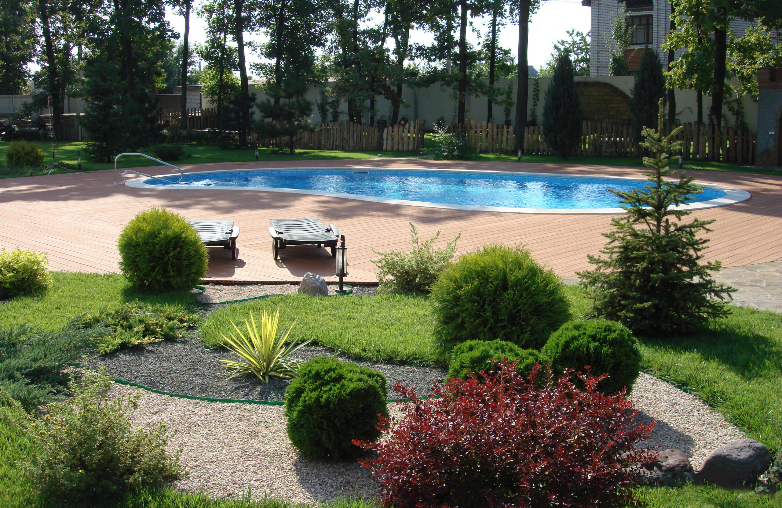 Bruggan Multicolor Cedar composite decking around an outdoor swimming pool in a landscaped garden