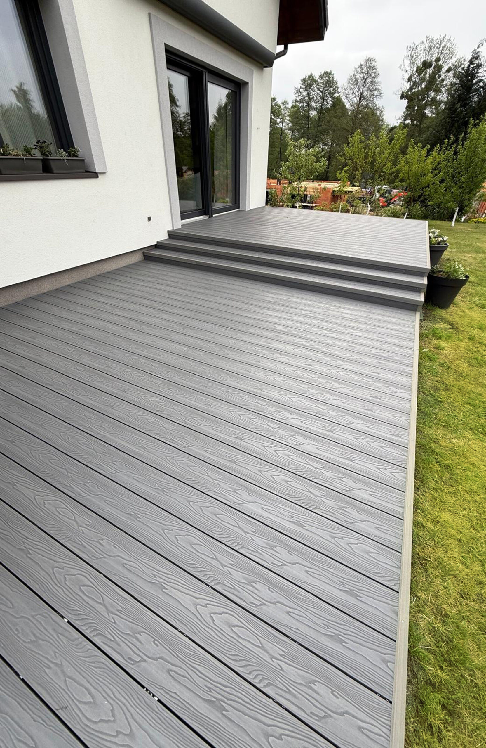 Bruggan Elegant Graphite composite decking terrace with steps next to a modern house and garden