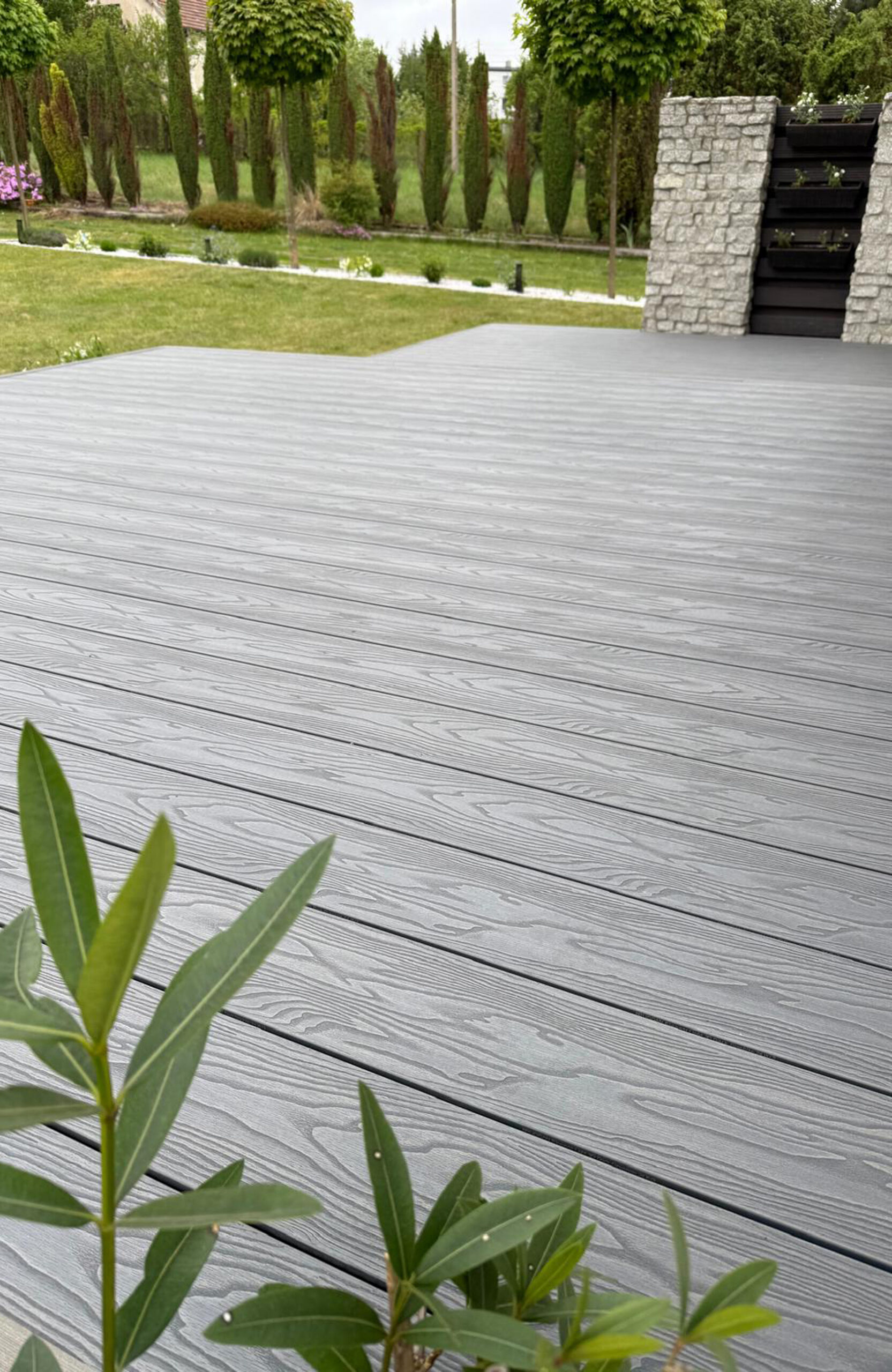 Spacious Bruggan Elegant Graphite composite deck surrounded by a landscaped green garden