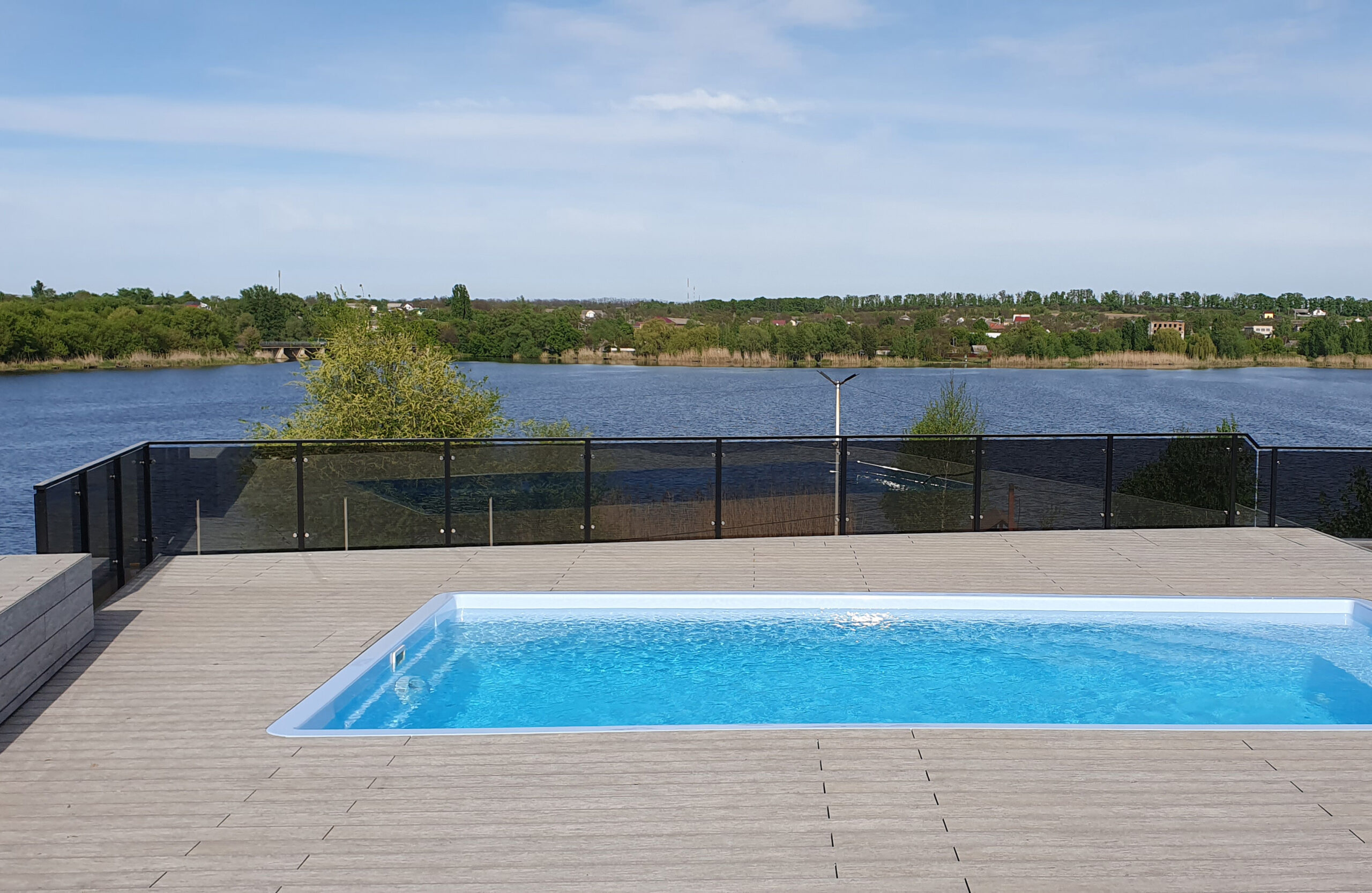 Outdoor swimming pool surrounded by BRUGGAN Multicolor grey composite decking in a waterfront landscape