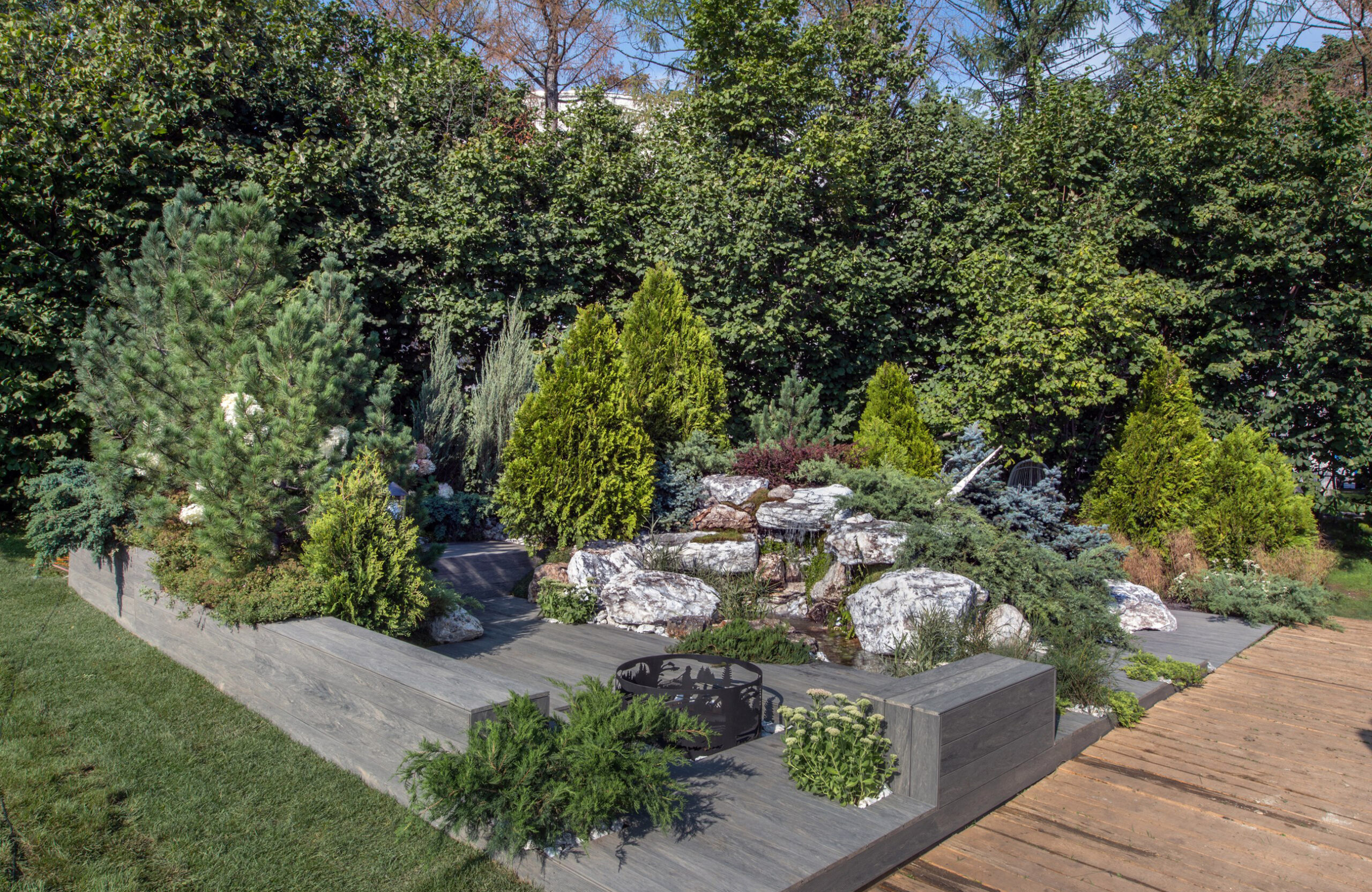 Landscaped outdoor area with BRUGGAN Multicolor grey composite decking, lush plants, rocks and water features