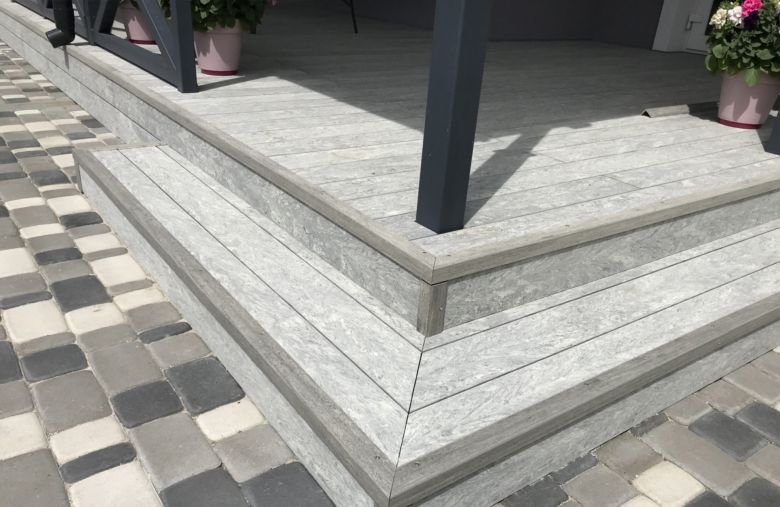 BRUGGAN Multicolor grey decking used for a stylish covered patio with integrated stairs and decorative railings.