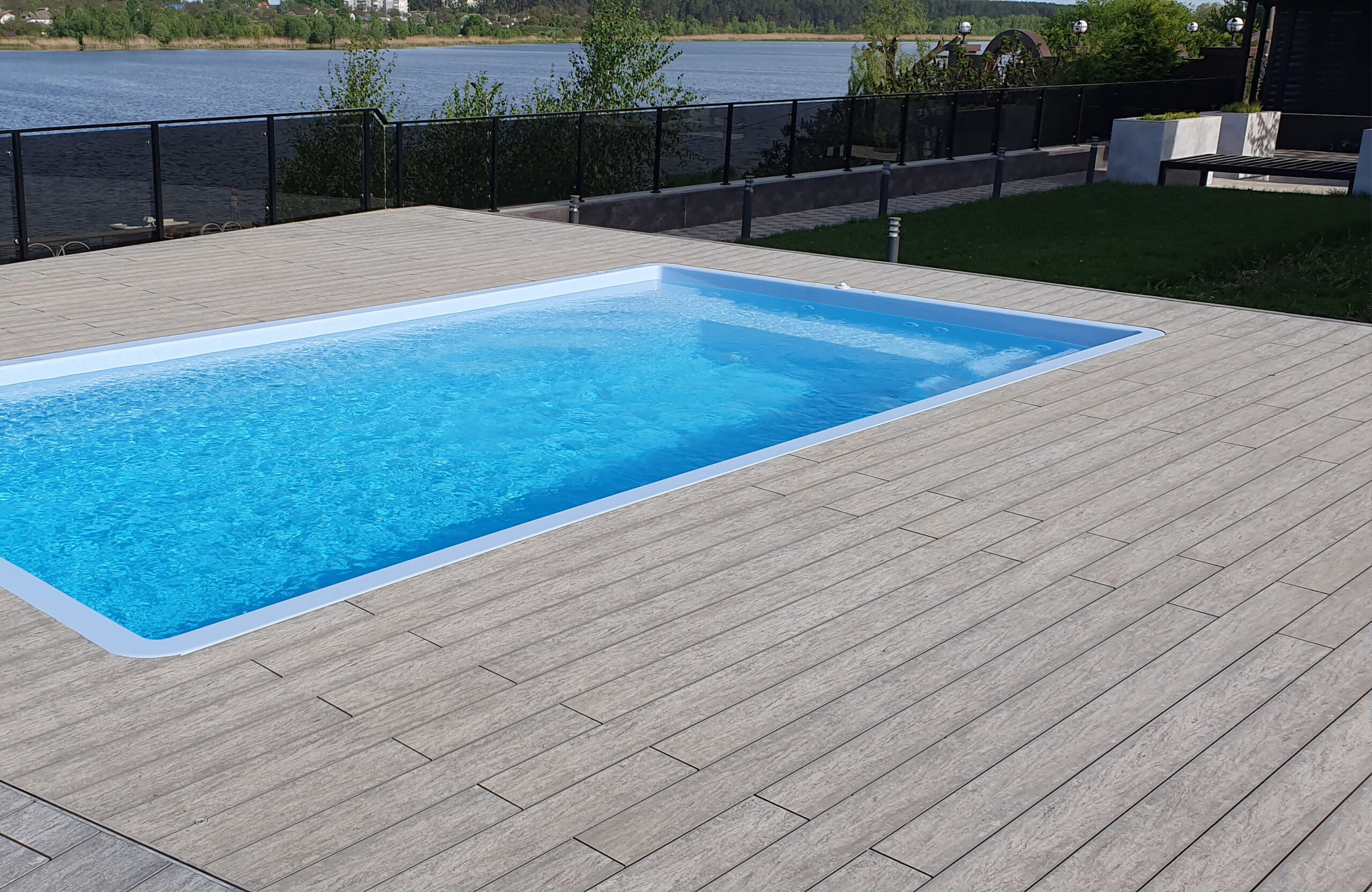 Outdoor swimming pool surrounded by BRUGGAN Multicolor grey composite decking in a waterfront landscape