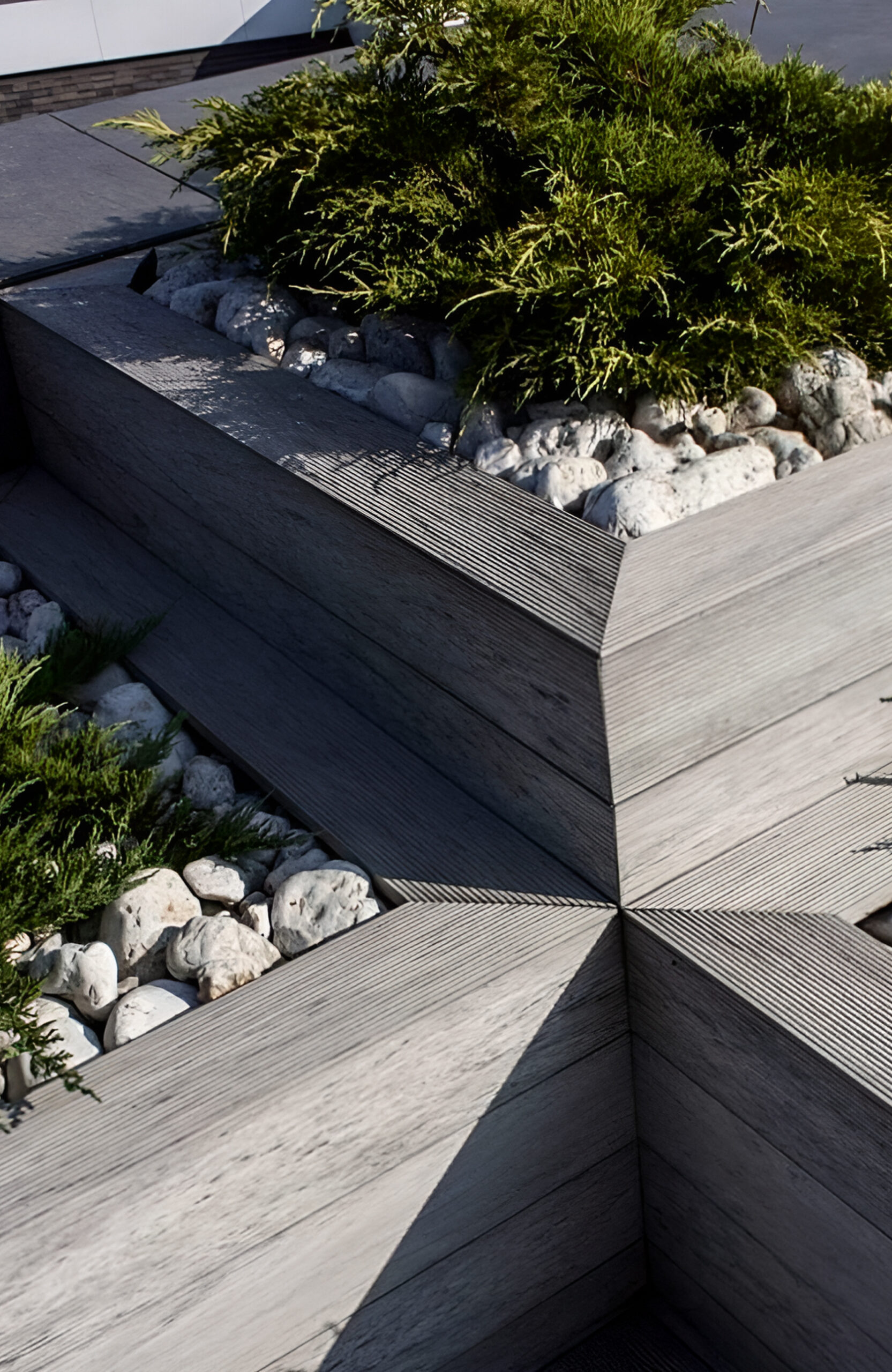 Landscaped outdoor area with BRUGGAN Multicolor grey composite decking, lush plants, rocks and water features