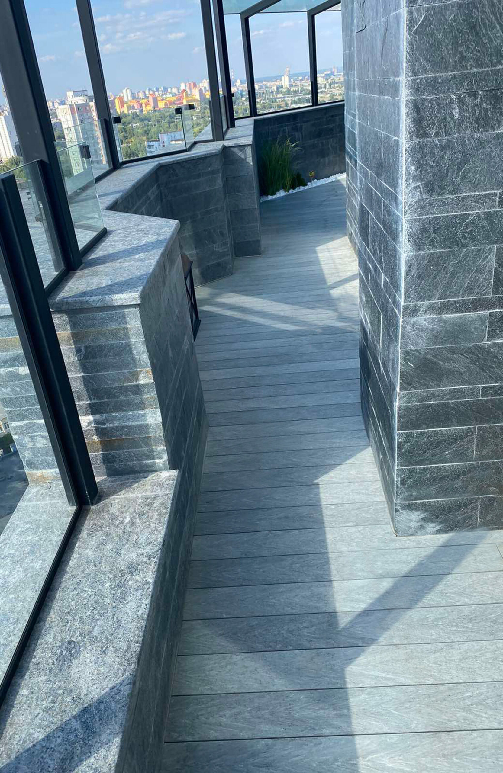 Urban balcony with BRUGGAN Multicolor grey composite decking, seating area and panoramic glazing