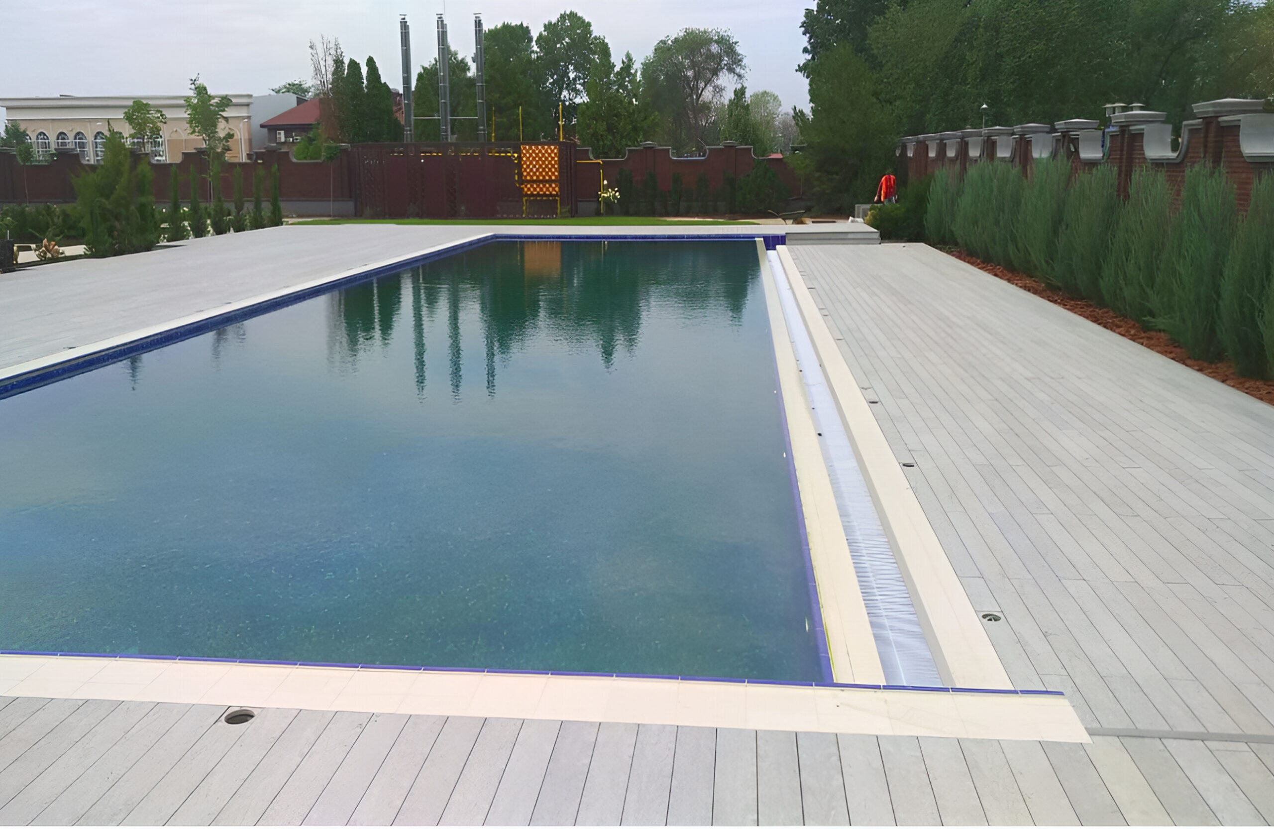BRUGGAN Multicolor grey composite decking installed around a large outdoor swimming pool