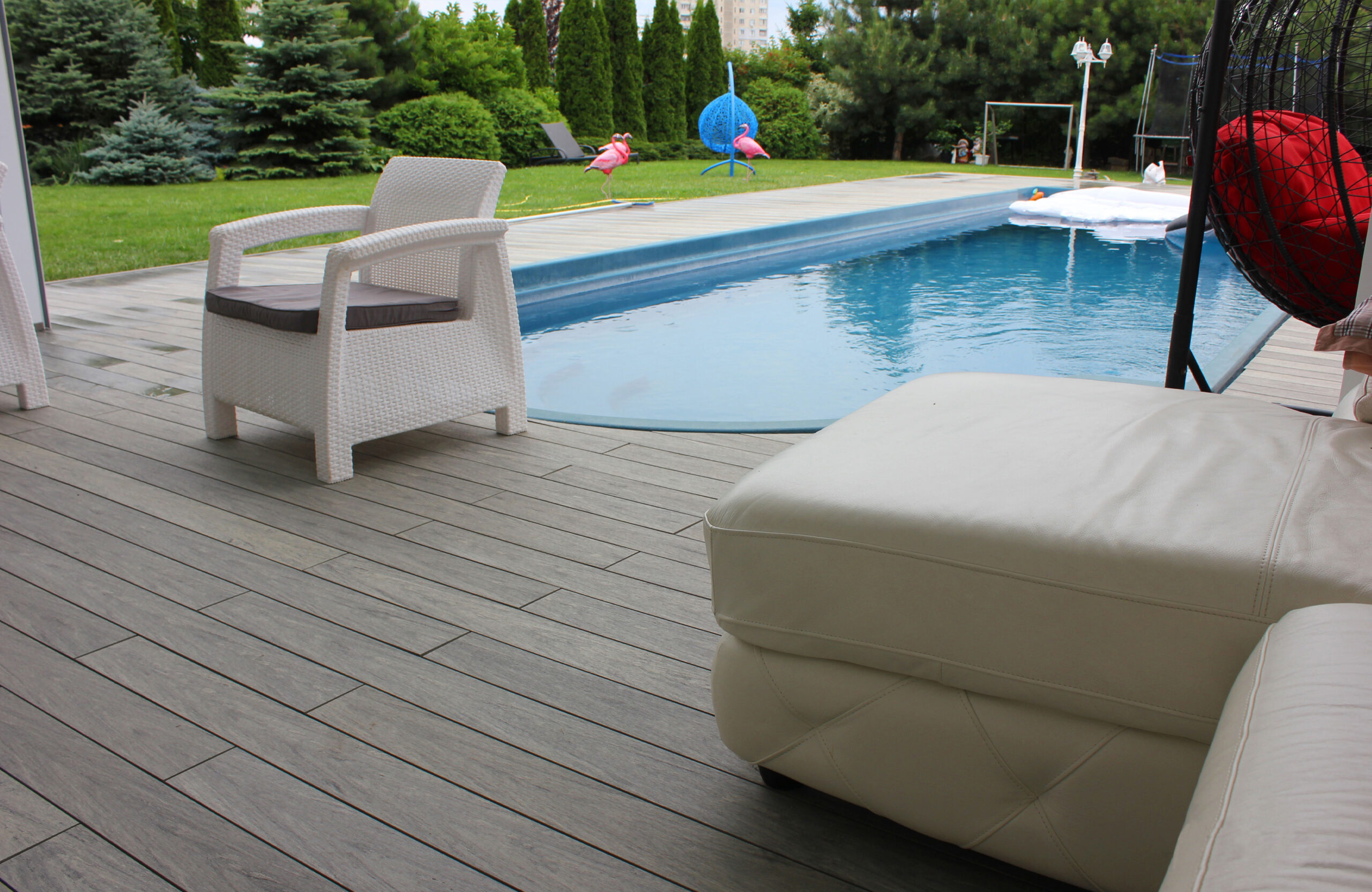 BRUGGAN Multicolor grey composite decking around a private outdoor swimming pool with a covered lounge area and garden