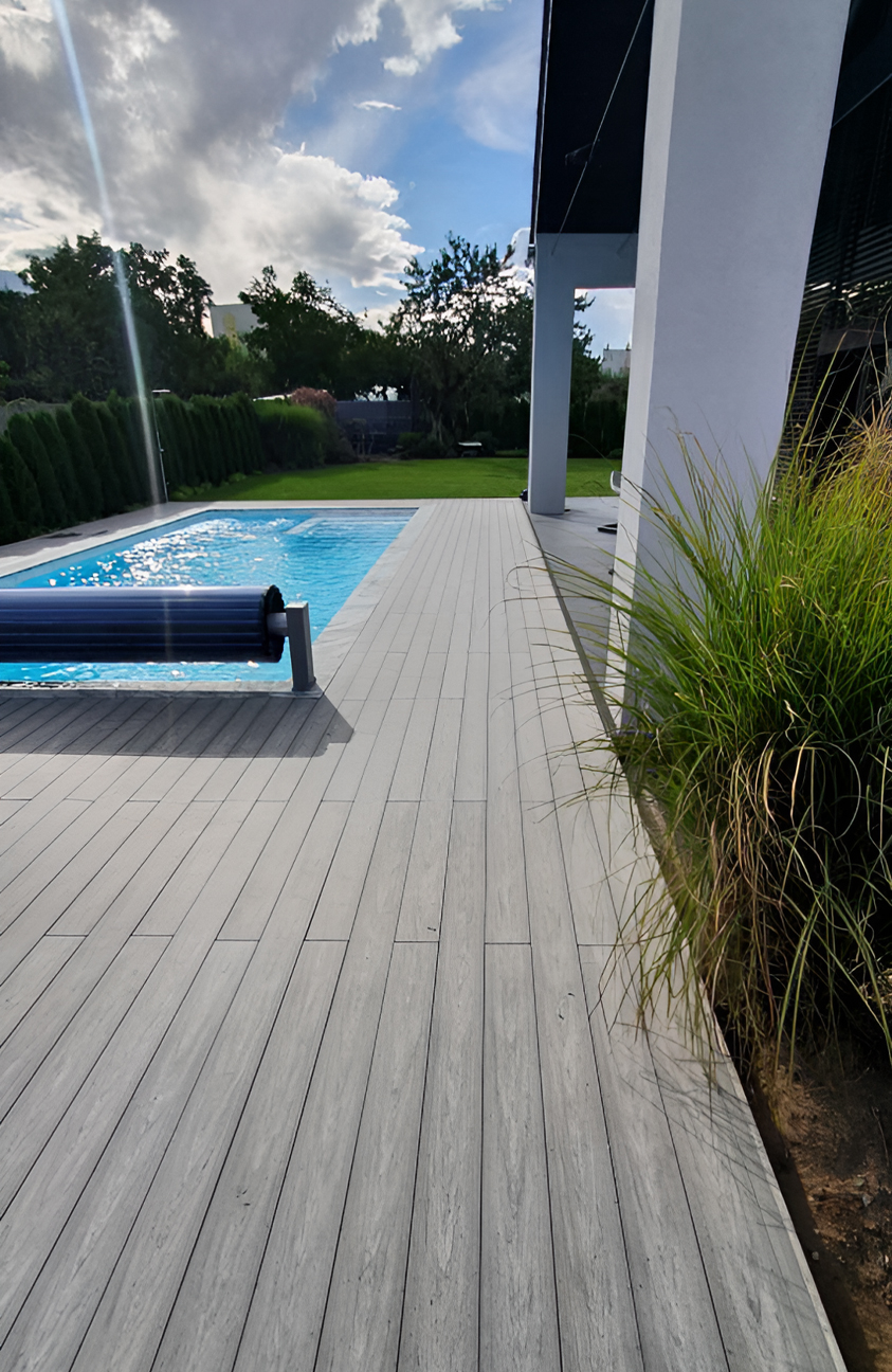 BRUGGAN Multicolor grey composite decking around a modern outdoor swimming pool and terrace in a landscaped private garden