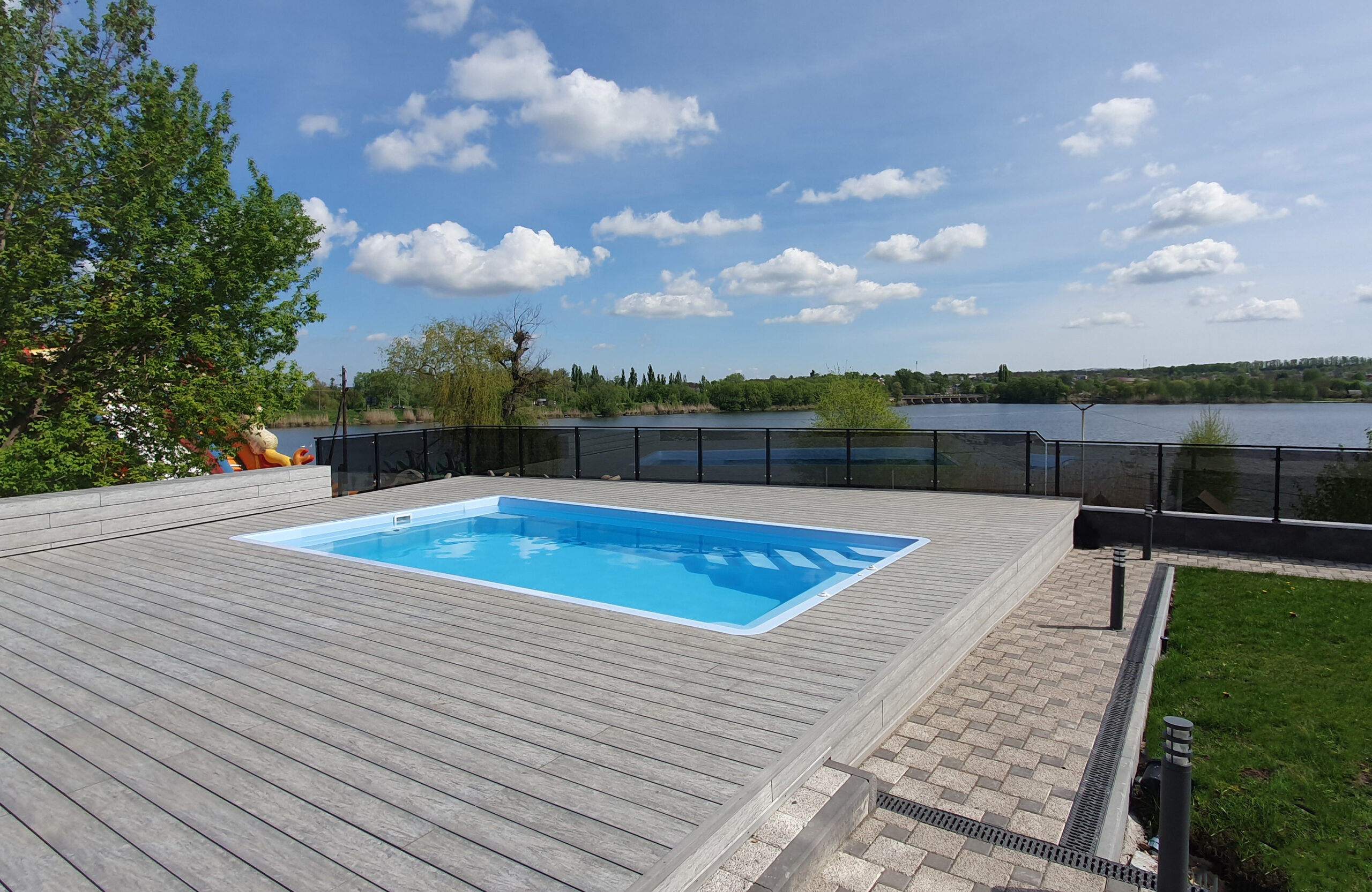 Outdoor swimming pool surrounded by BRUGGAN Multicolor grey composite decking in a waterfront landscape