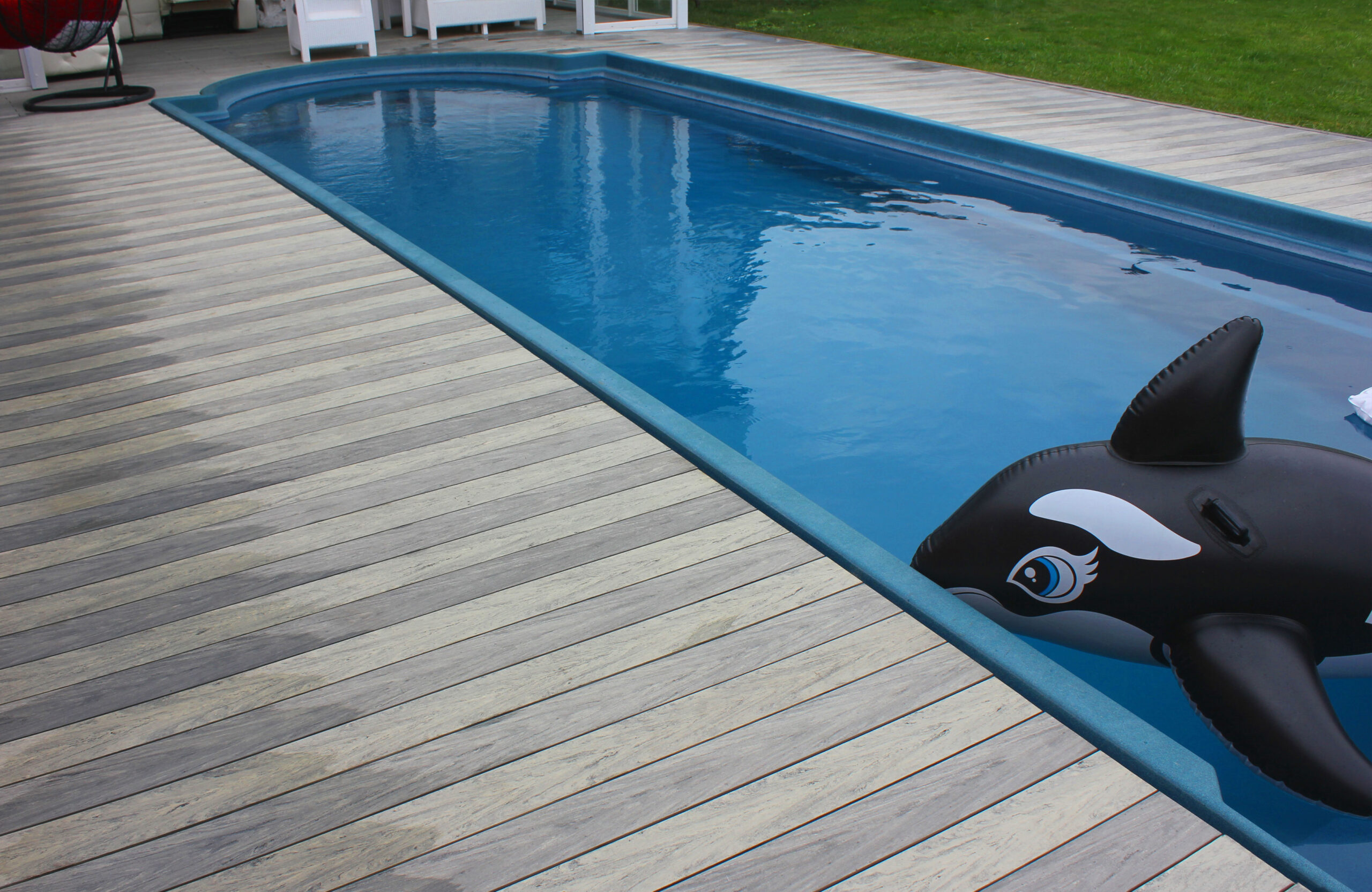 BRUGGAN Multicolor grey composite decking around a private outdoor swimming pool with a covered lounge area and garden