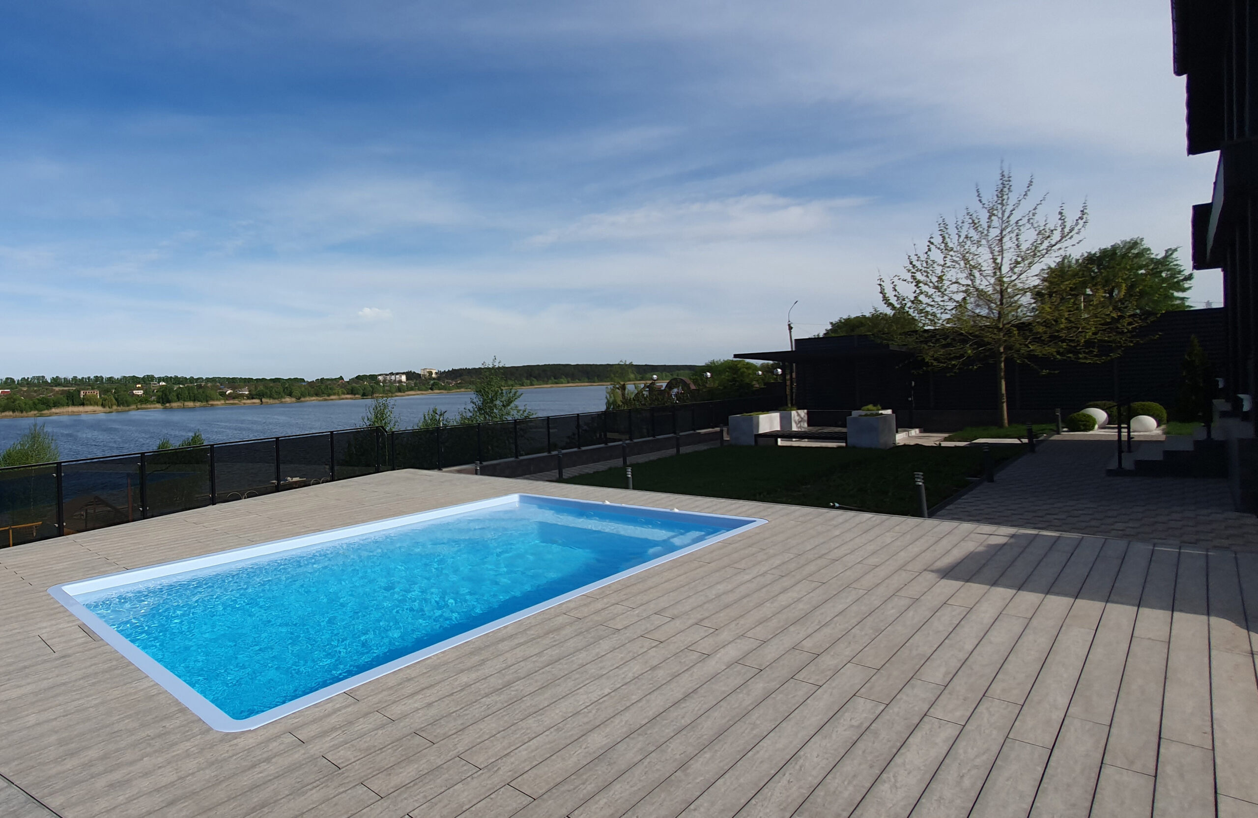 Outdoor swimming pool surrounded by BRUGGAN Multicolor grey composite decking in a waterfront landscape