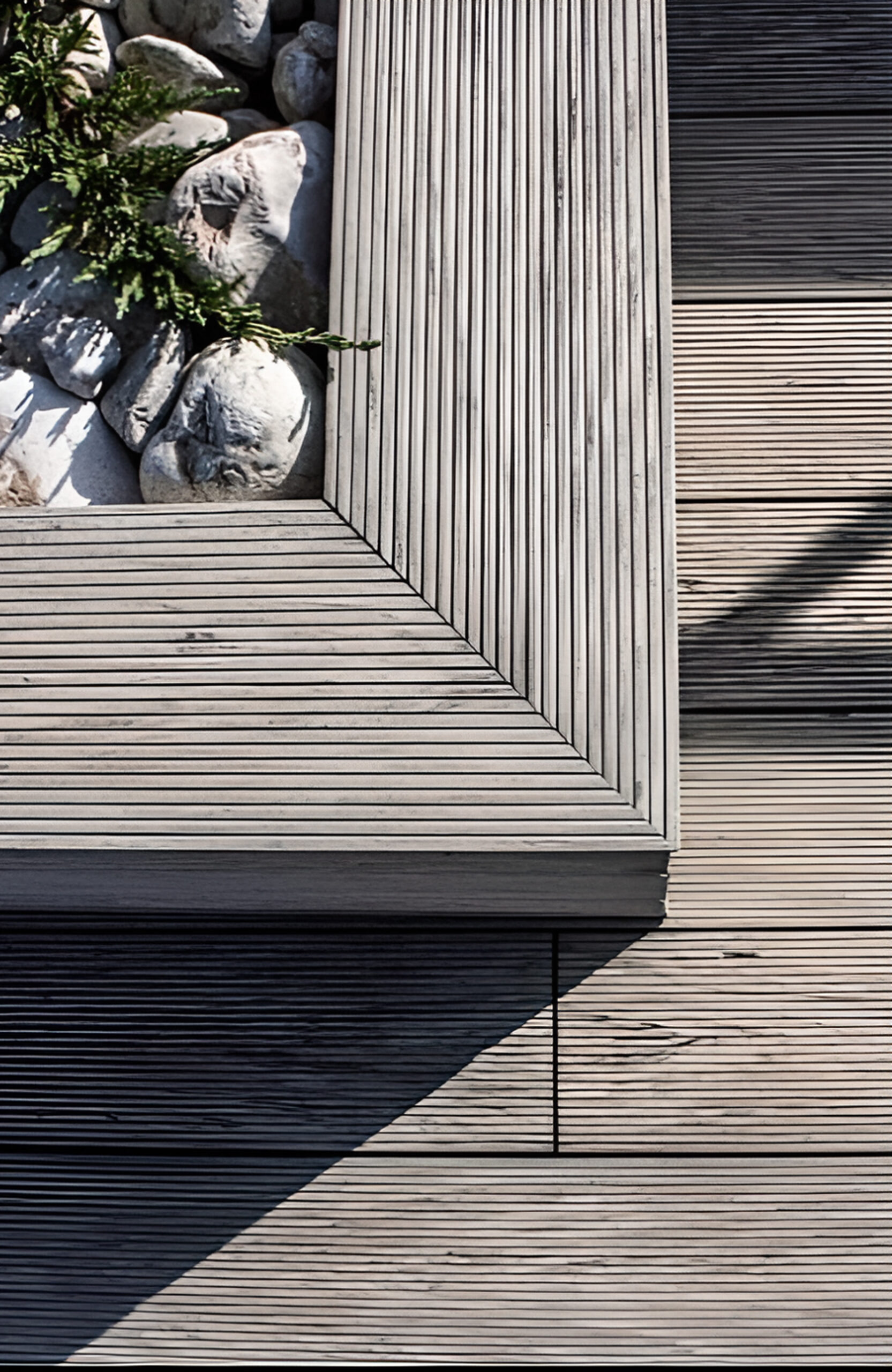 Landscaped outdoor area with BRUGGAN Multicolor grey composite decking, lush plants, rocks and water features