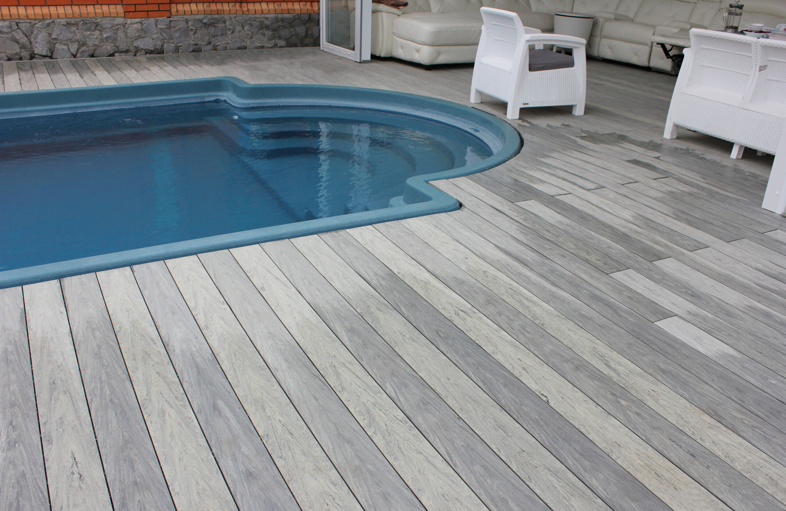 BRUGGAN Multicolor grey composite decking around a private outdoor swimming pool with a covered lounge area and garden
