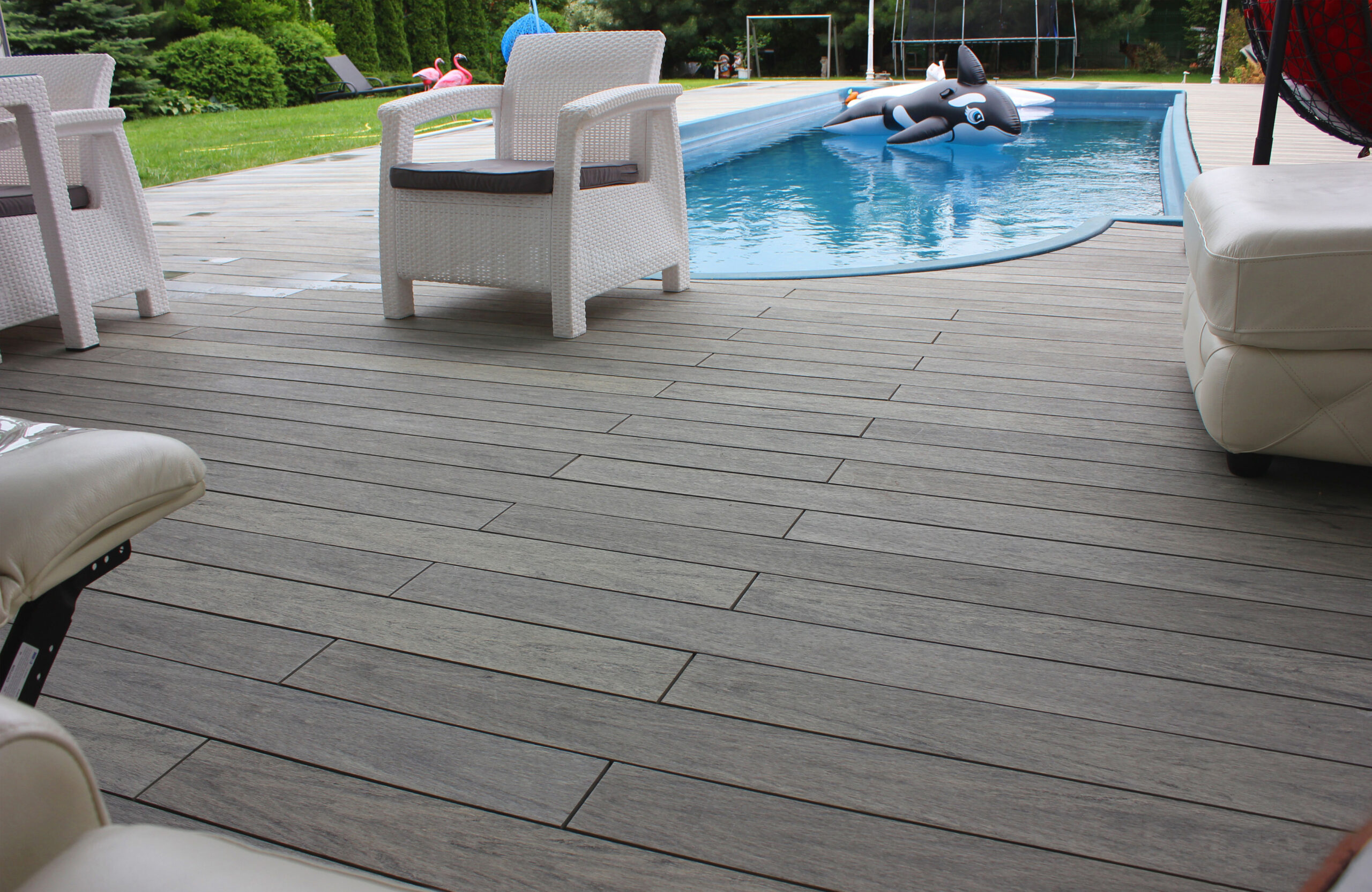 BRUGGAN Multicolor grey composite decking around a private outdoor swimming pool with a covered lounge area and garden