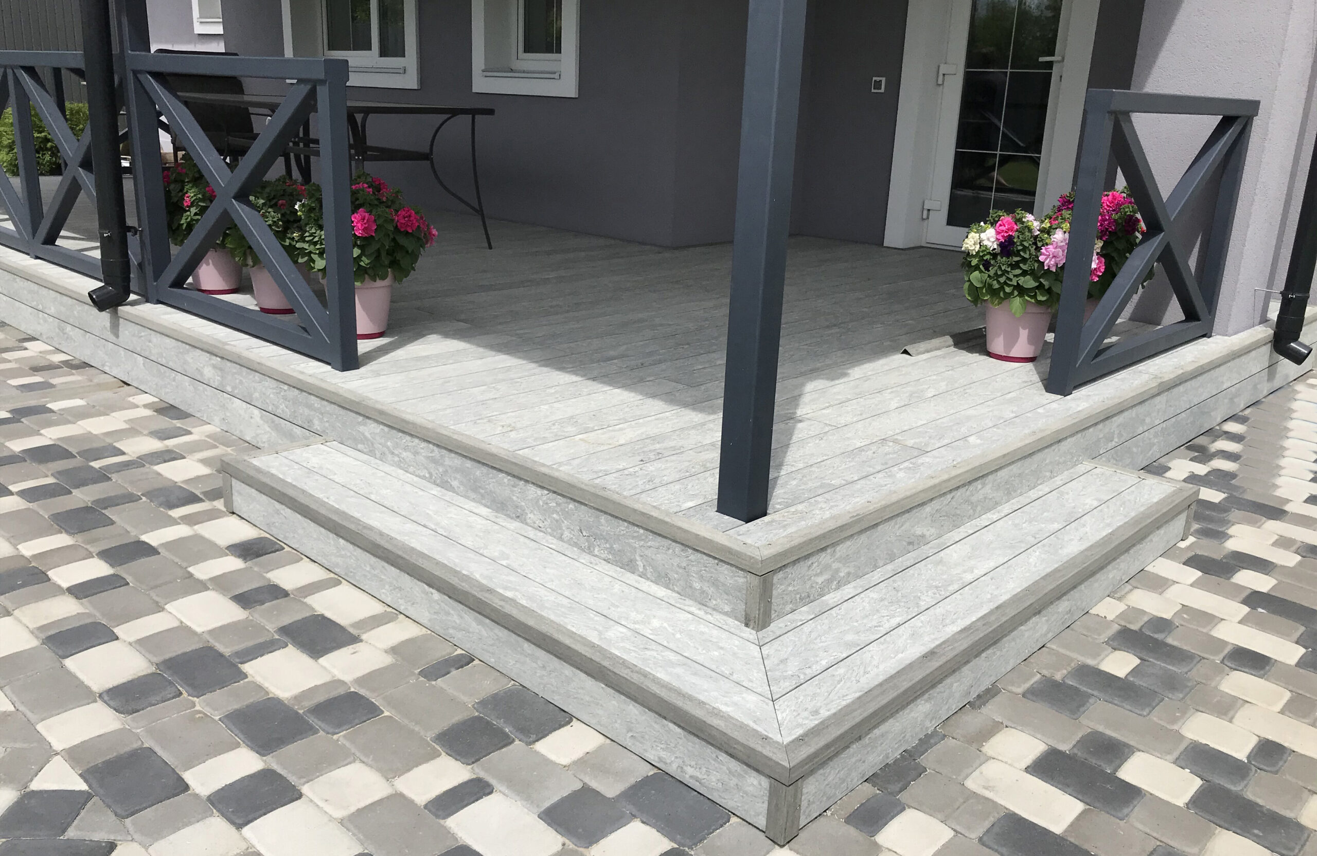 BRUGGAN Multicolor grey decking used for a stylish covered patio with integrated stairs and decorative railings.