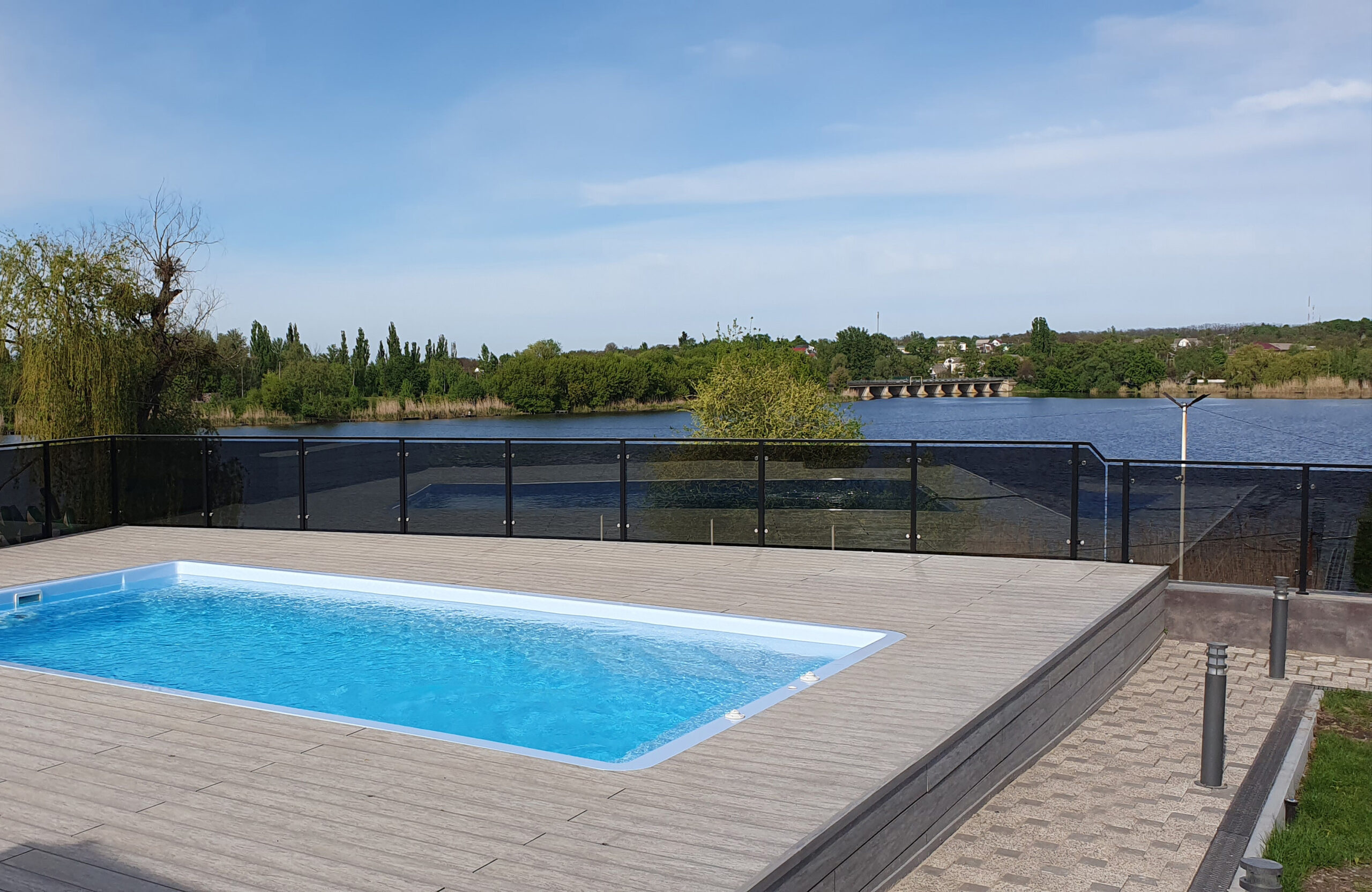 Outdoor swimming pool surrounded by BRUGGAN Multicolor grey composite decking in a waterfront landscape