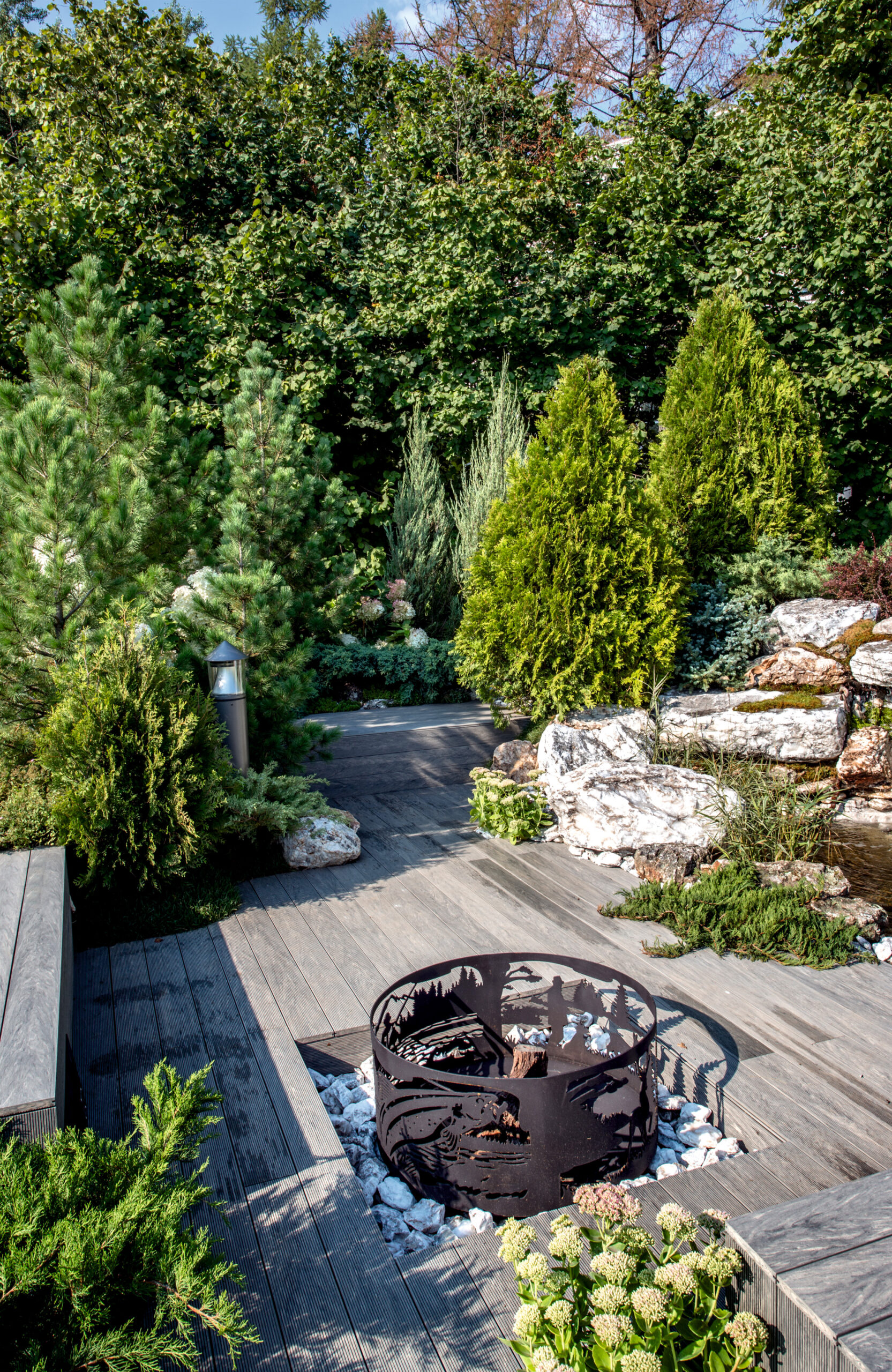 Landscaped outdoor area with BRUGGAN Multicolor grey composite decking, lush plants, rocks and water features