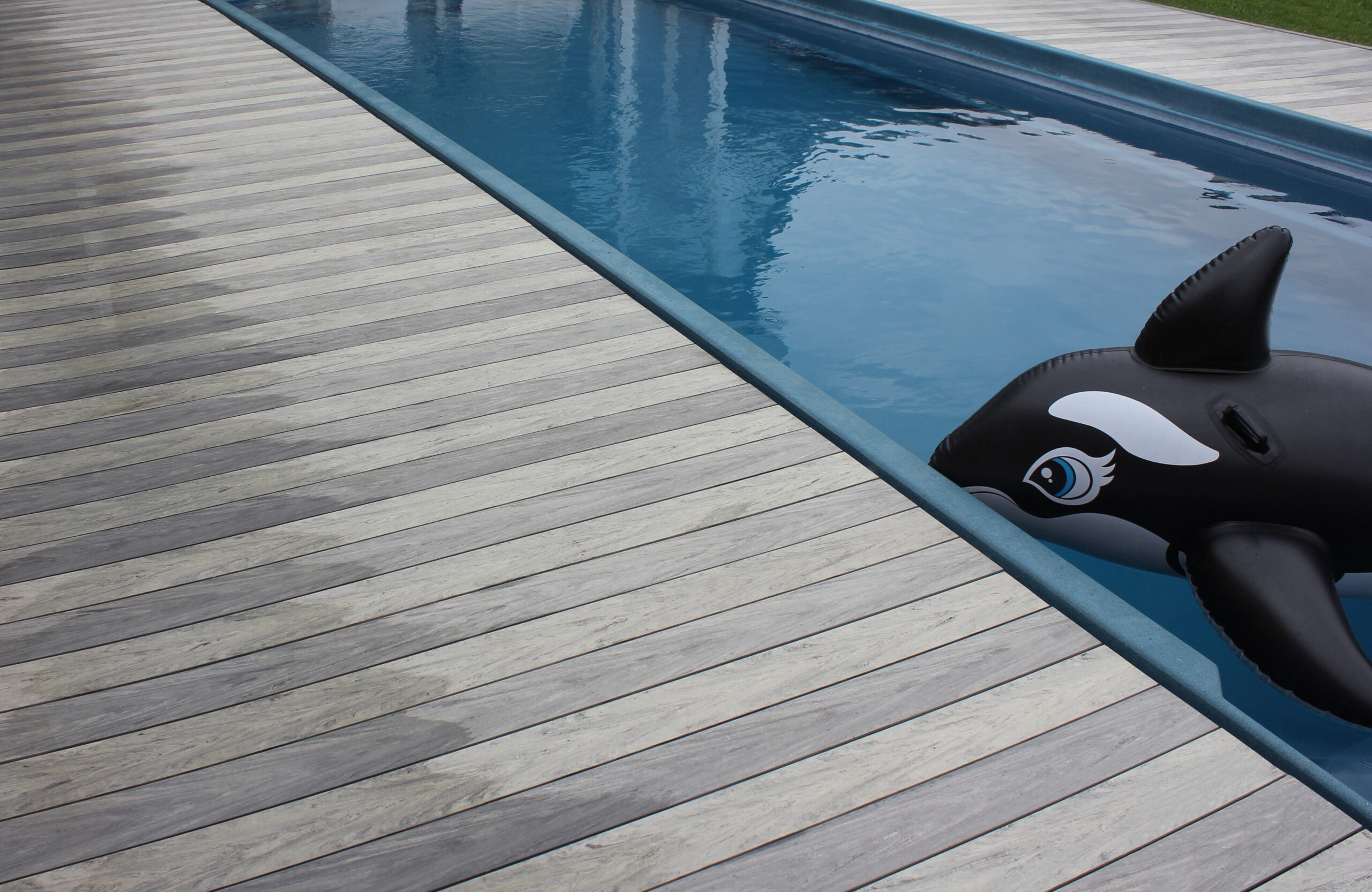 BRUGGAN Multicolor grey composite decking around a private outdoor swimming pool with a covered lounge area and garden