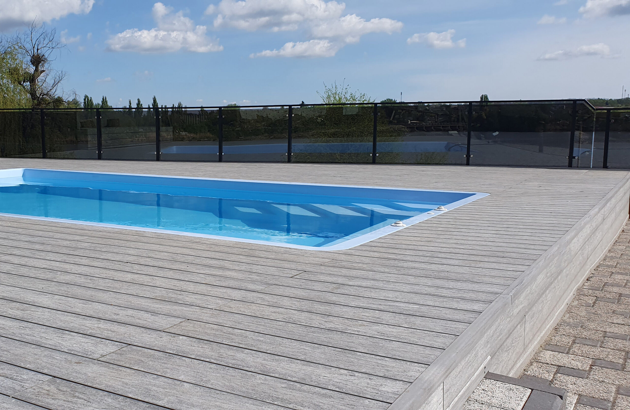 Outdoor swimming pool surrounded by BRUGGAN Multicolor grey composite decking in a waterfront landscape