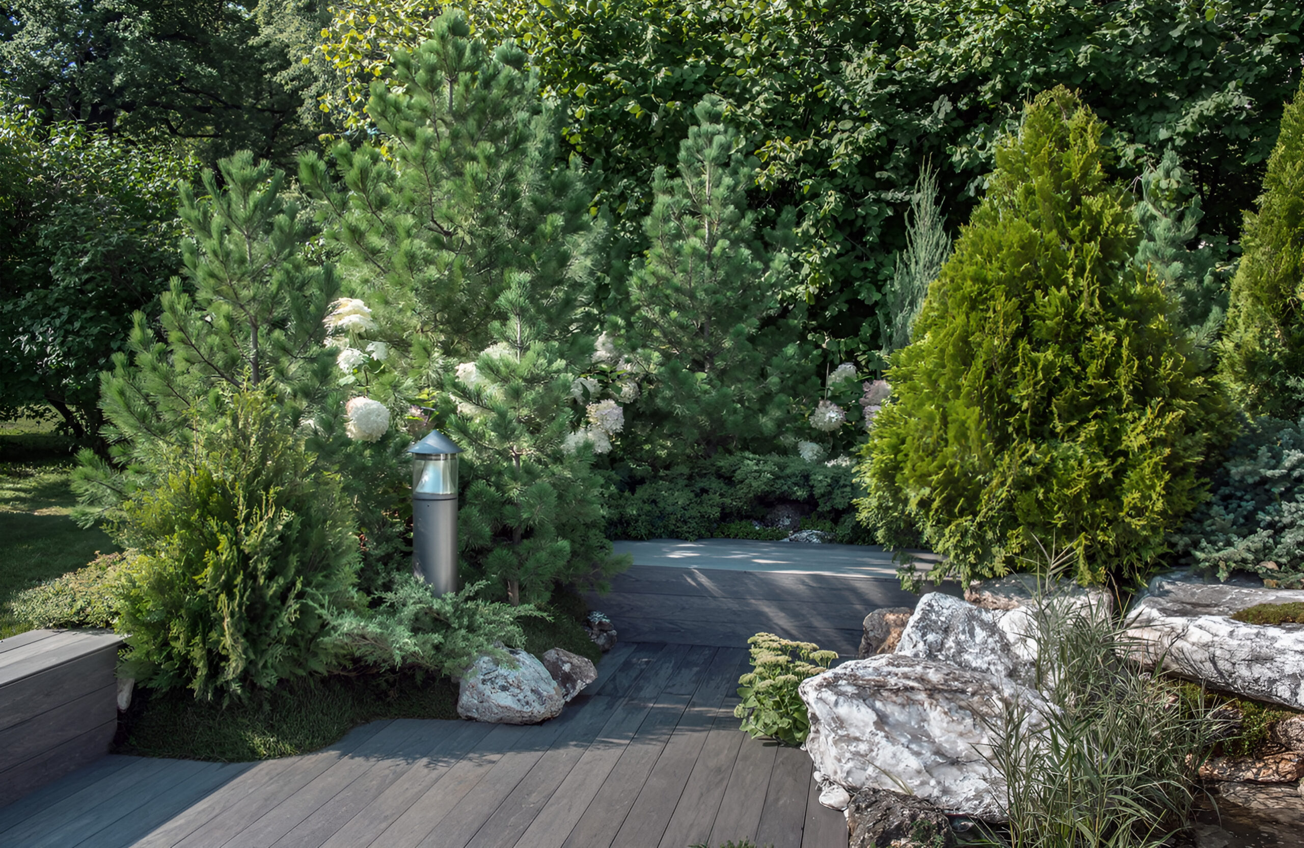 Landscaped outdoor area with BRUGGAN Multicolor grey composite decking, lush plants, rocks and water features