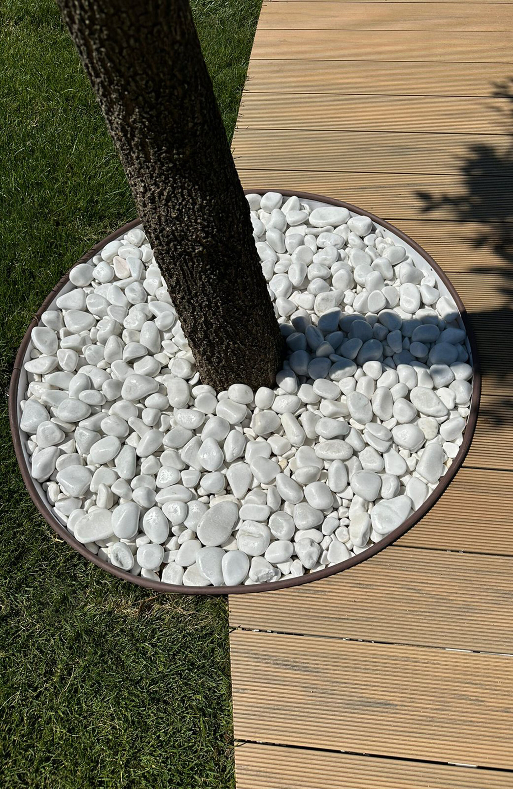 Sand-colored BRUGGAN Multicolor composite decking surrounding a garden pool with trees and lawn