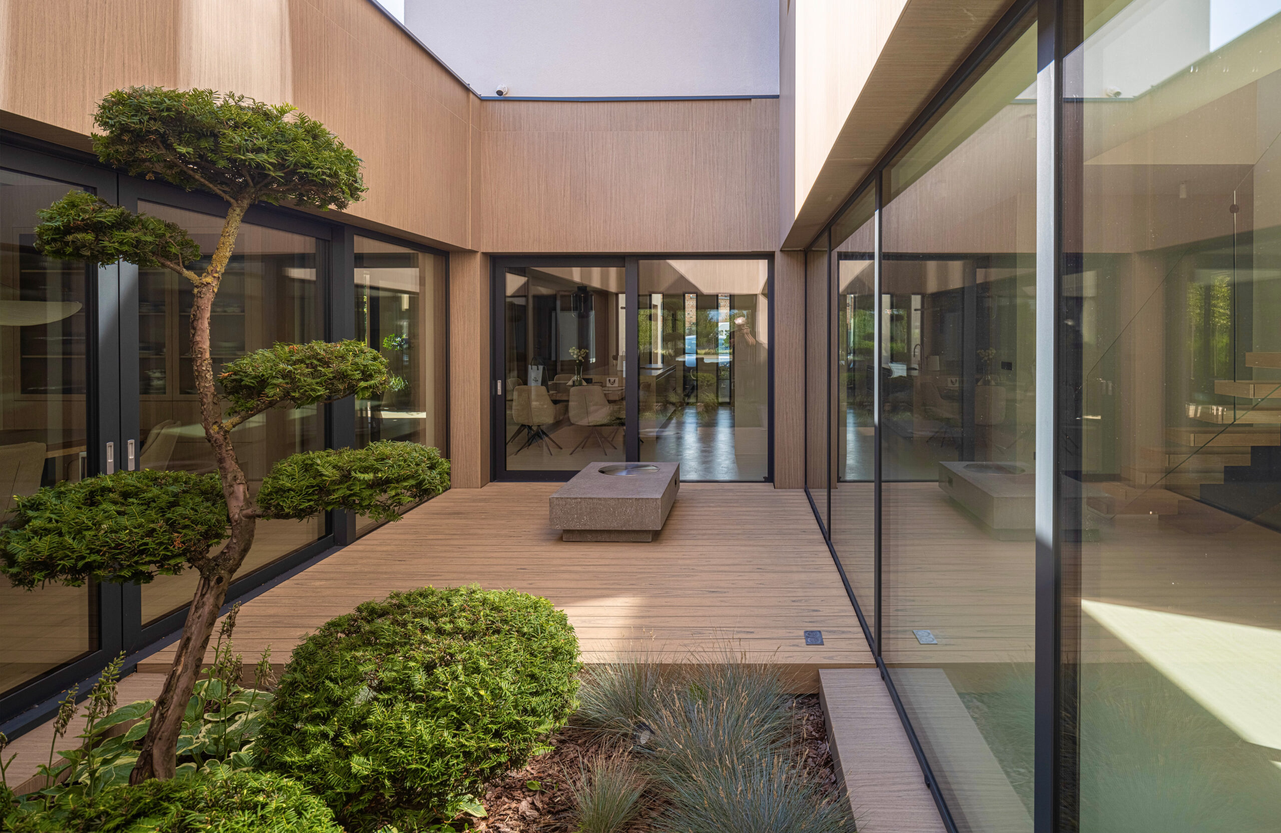 Sand-colored BRUGGAN Multicolor composite decking in a contemporary inner courtyard with panoramic glazing
