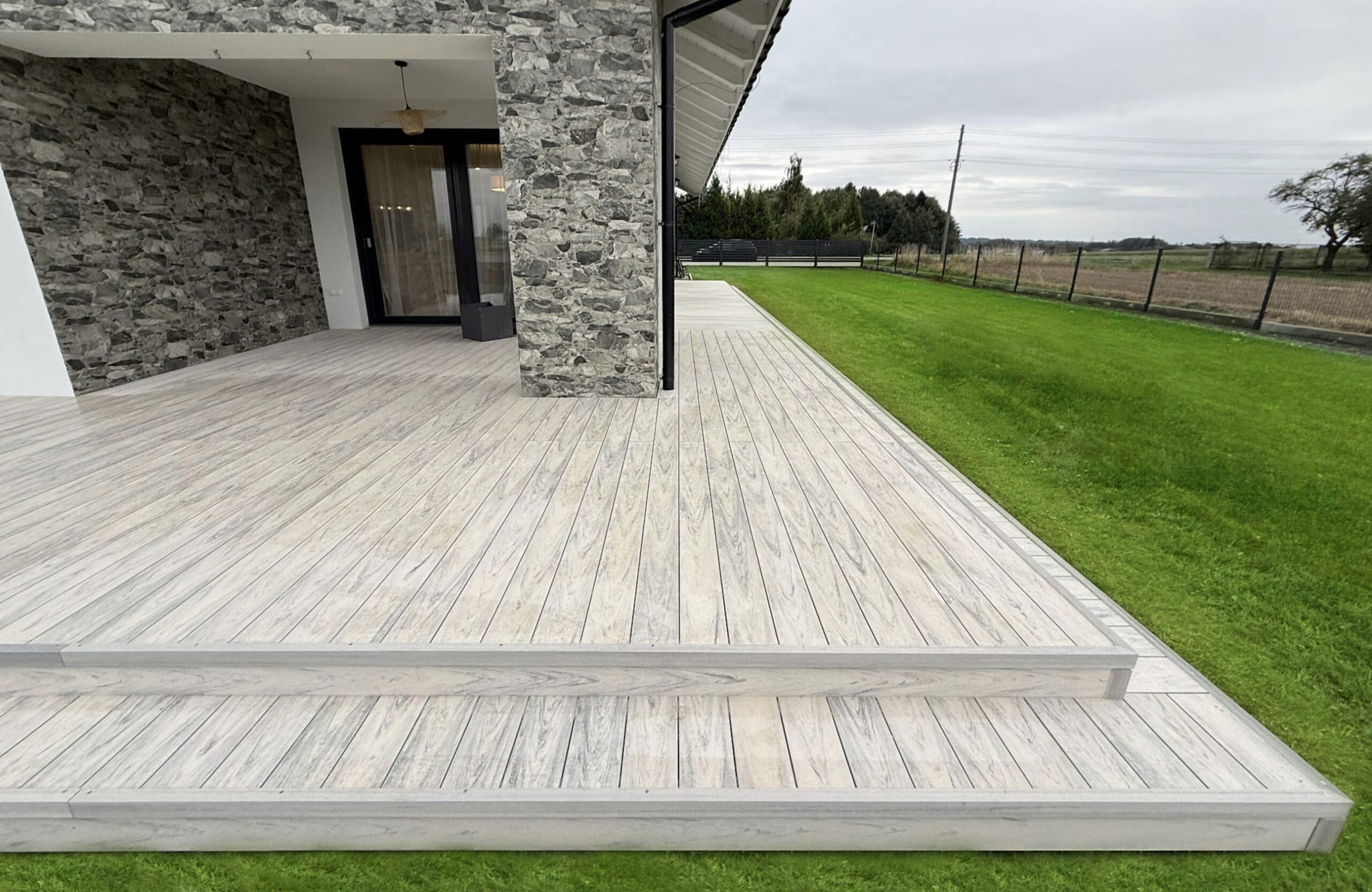 Light grey wood-effect composite decking with steps around a private home
