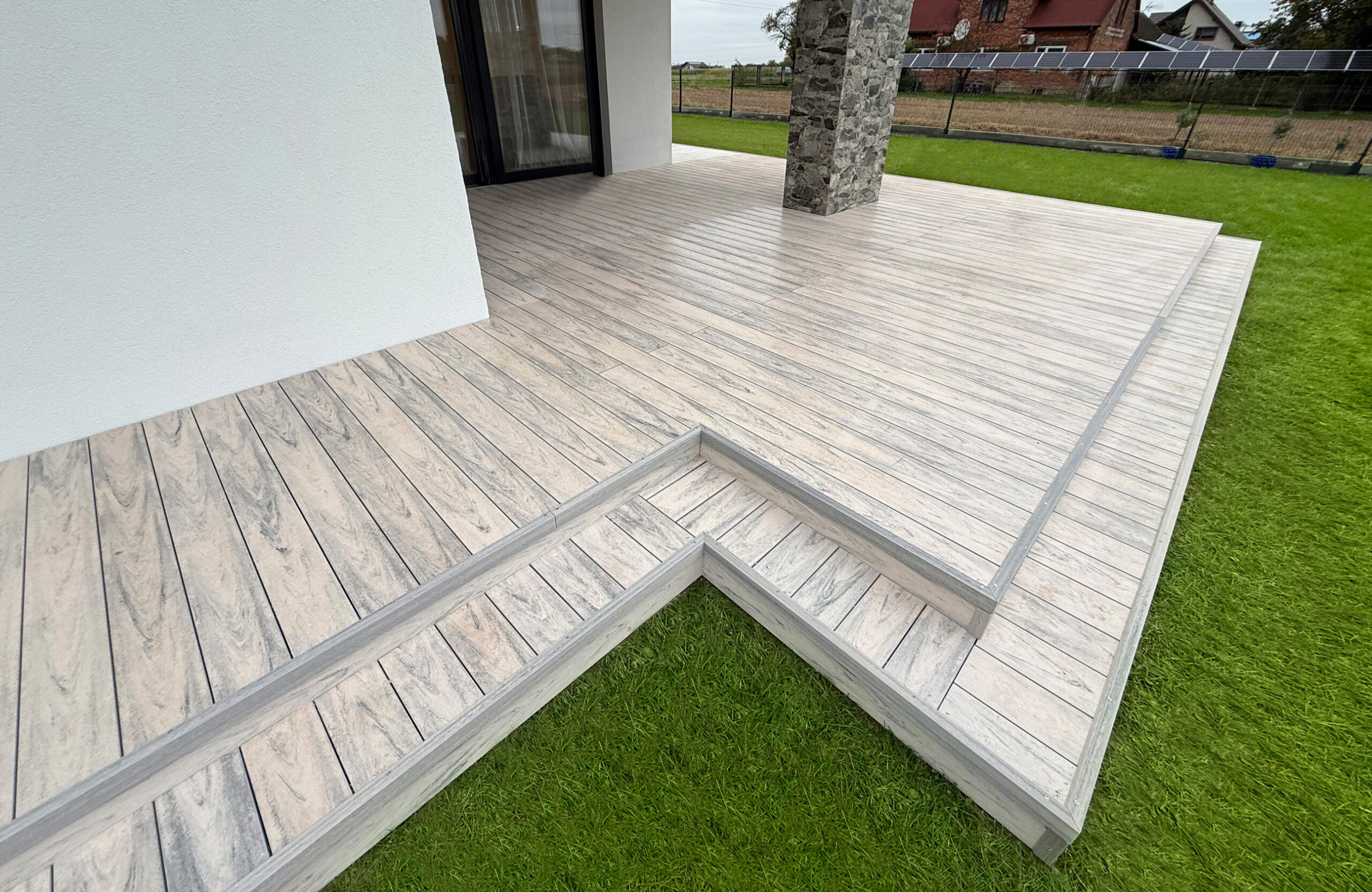Light grey wood-effect composite decking with steps around a private home