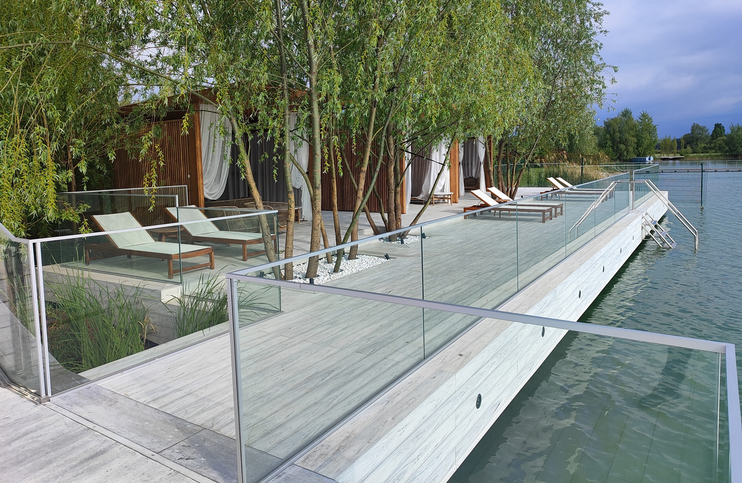 Modern lakeside terrace with light composite decking, lounge areas and glass railing