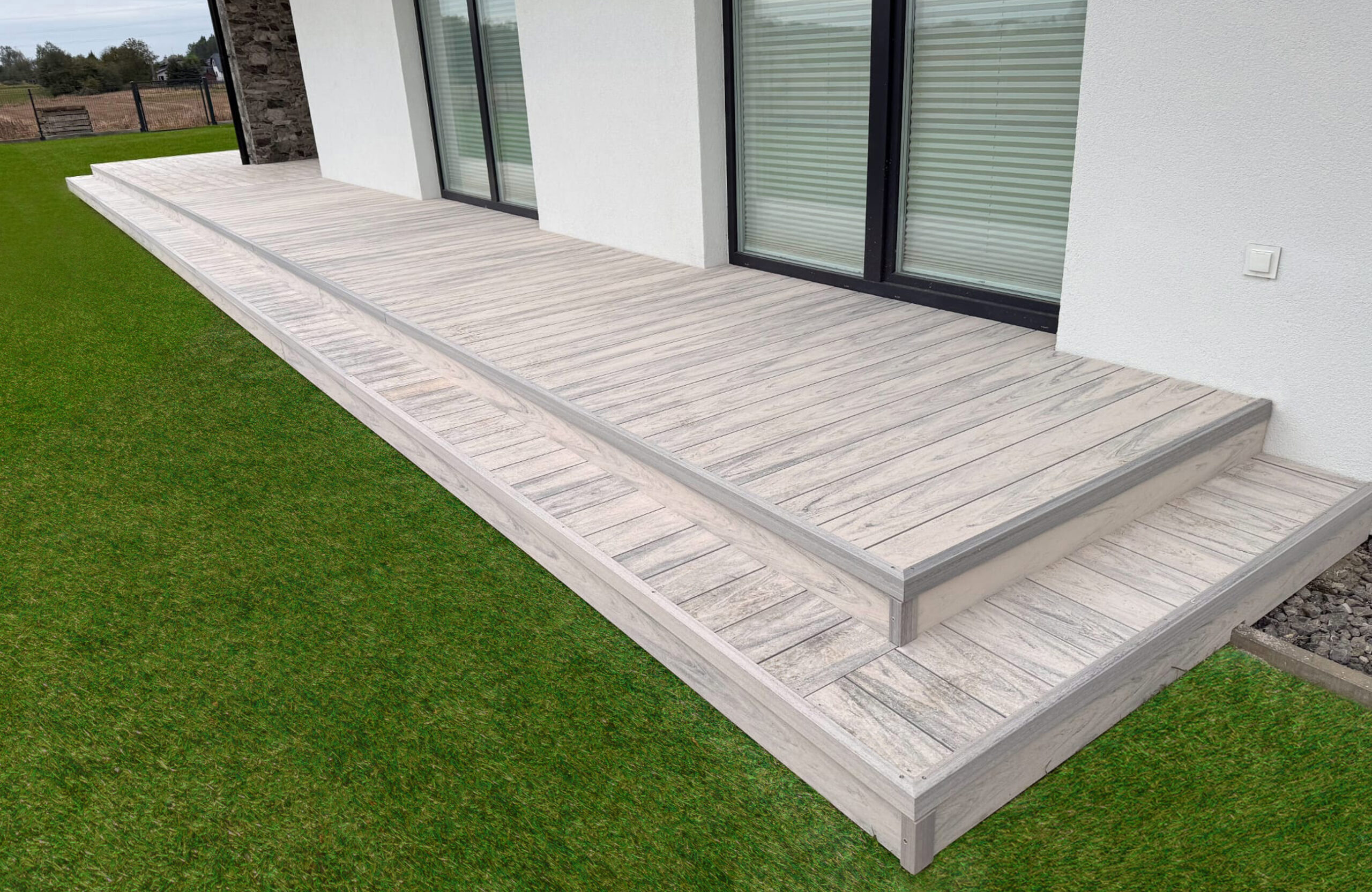 Light grey wood-effect composite decking with steps around a private home
