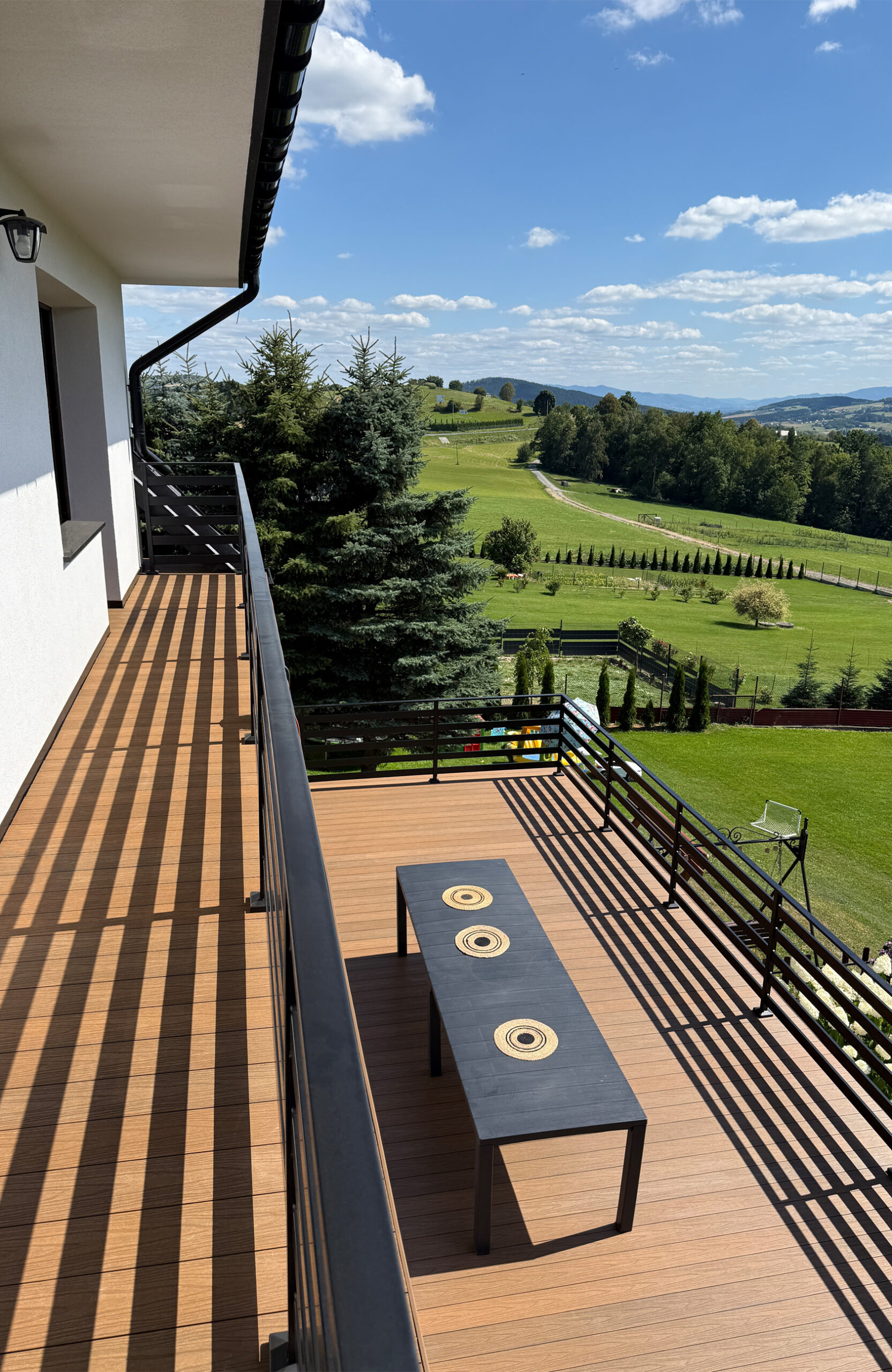 Durable and anti-slip composite decking installed on a large balcony, offering a stunning panoramic view of a mountain landscape on a sunny day.
