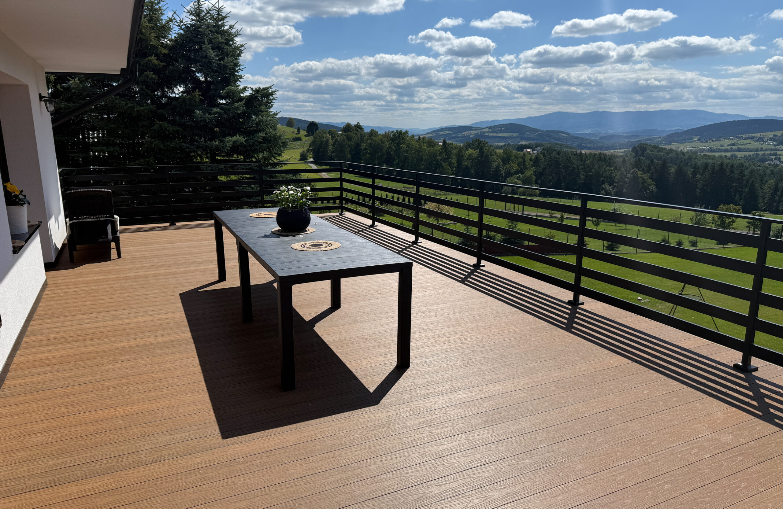 Low-maintenance composite decking creates a modern and functional outdoor living space, featuring a cozy seating area with a table, plant, and spectacular mountain views.